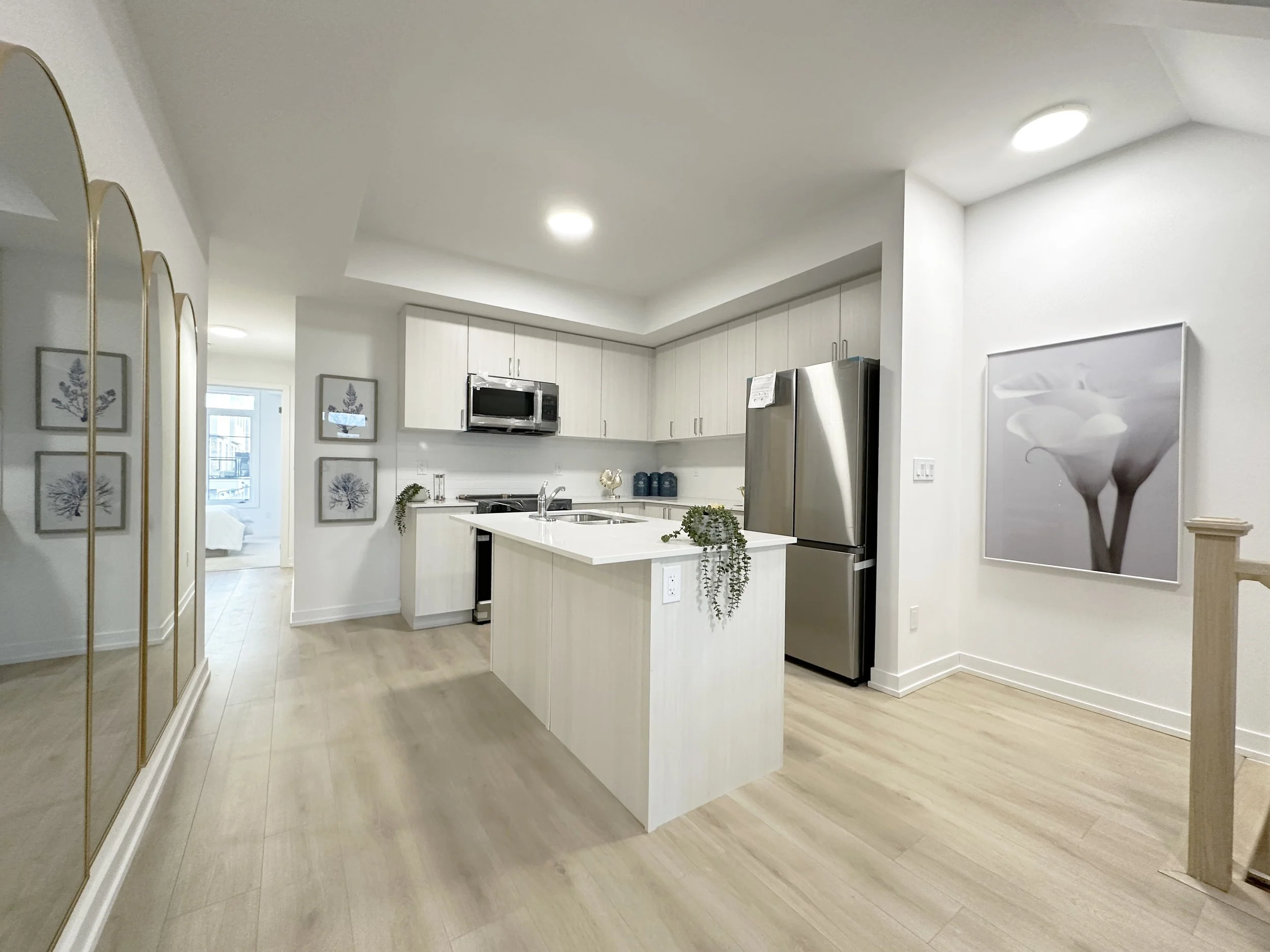 Modern kitchen with white cabinets, stainless steel appliances, a kitchen island, light wooden floors, and wall art around the space.
