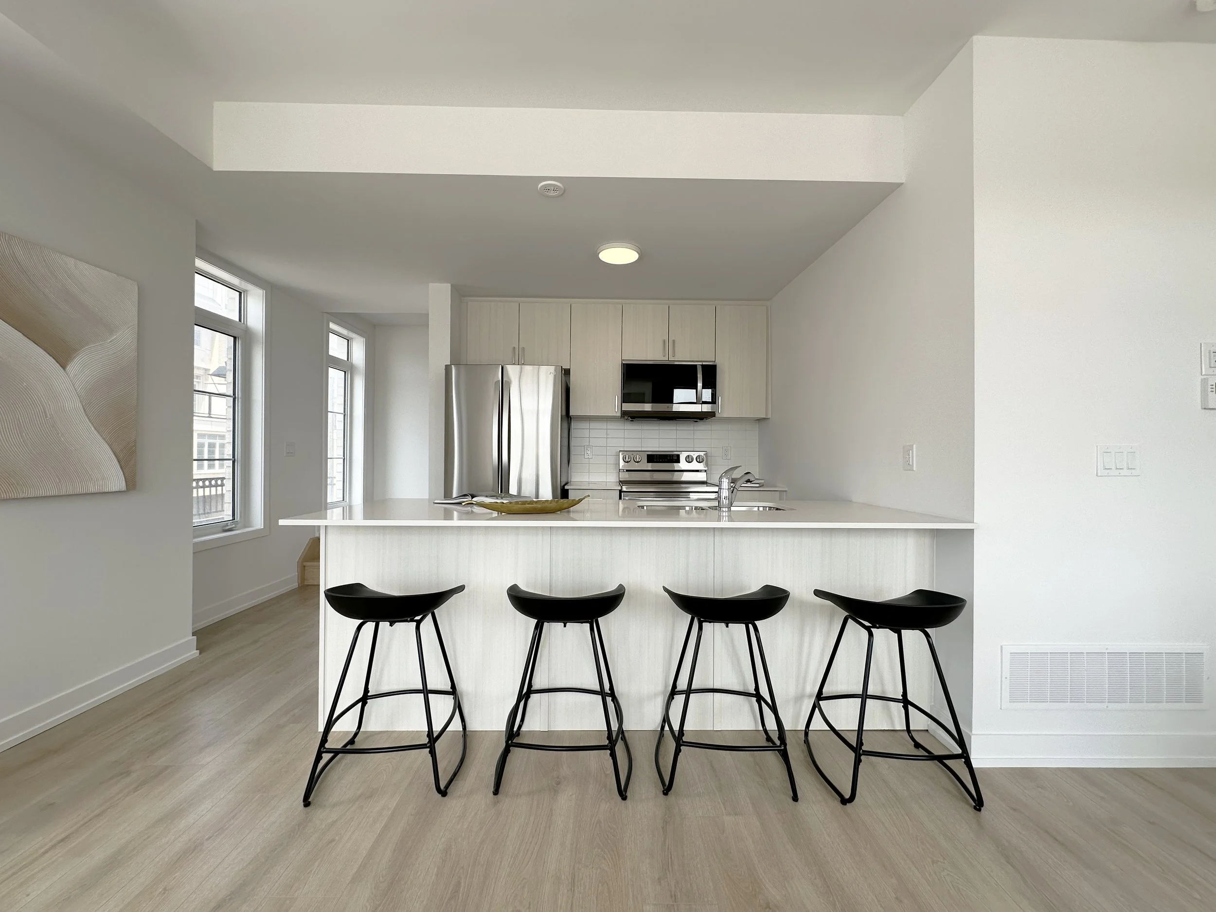 Modern kitchen with white cabinets, stainless steel refrigerator, microwave, stove, white subway tile backsplash, and a white kitchen island with black chairs.