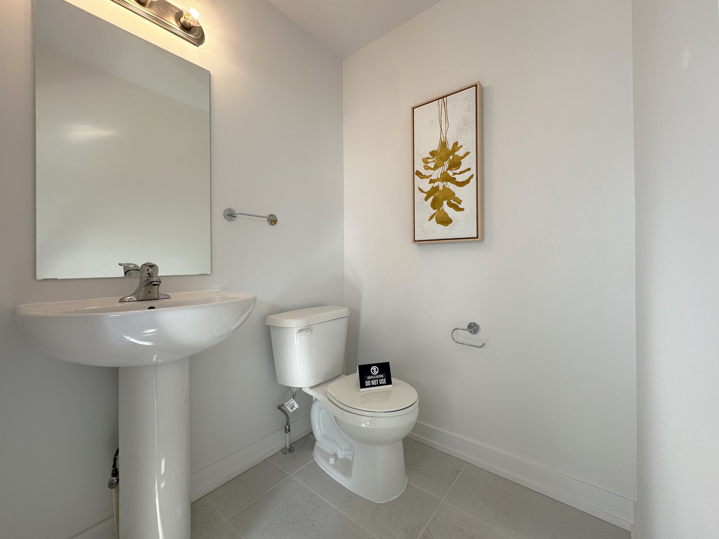 A small bathroom with a white sink on the left, a mirror above the sink, a white toilet with a 