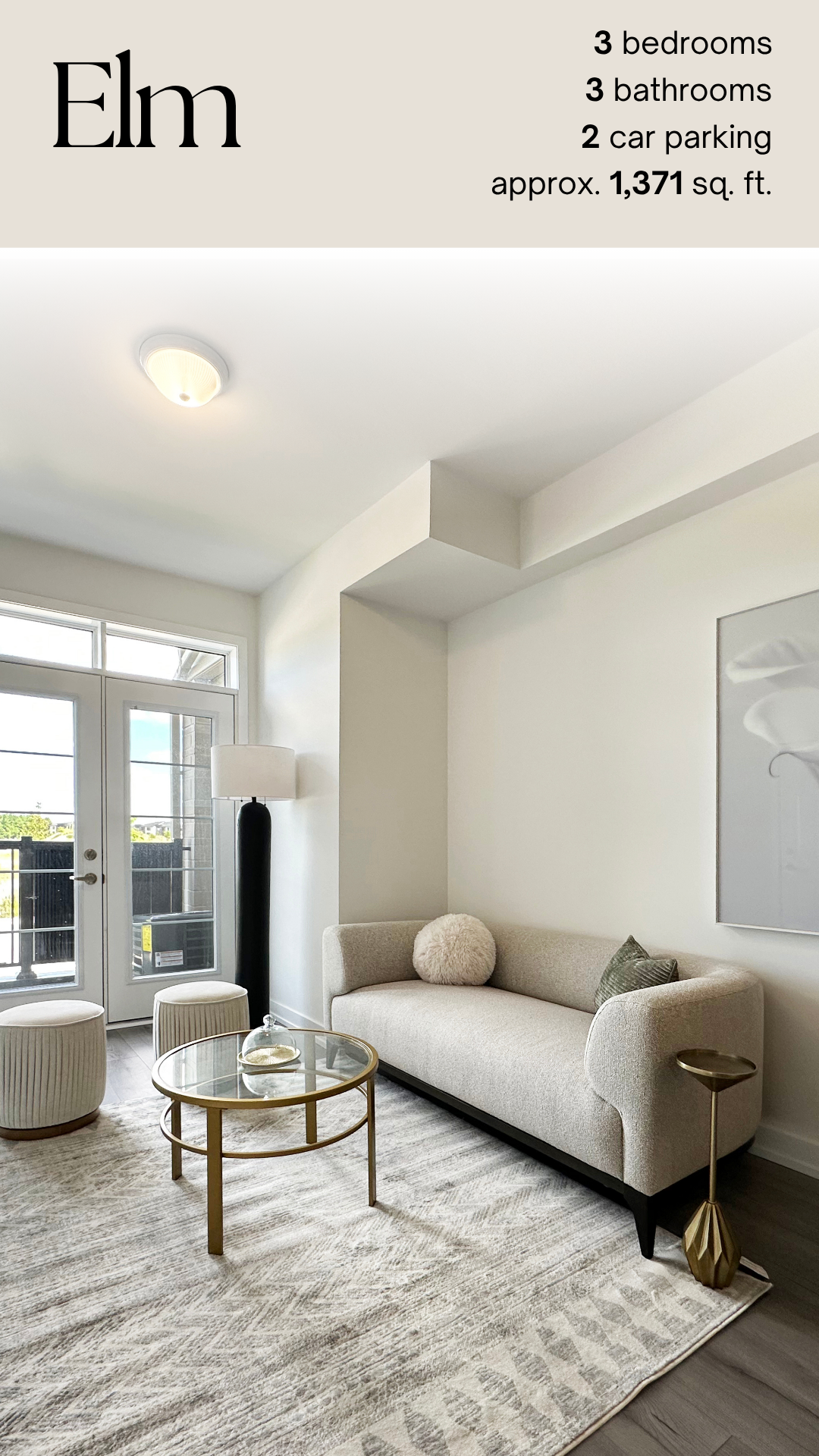 A modern living room with white walls, a beige sofa with a round pillow, a glass coffee table, two matching ottomans, a tall black floor lamp, a large framed artwork, and glass doors leading to an outdoor balcony.