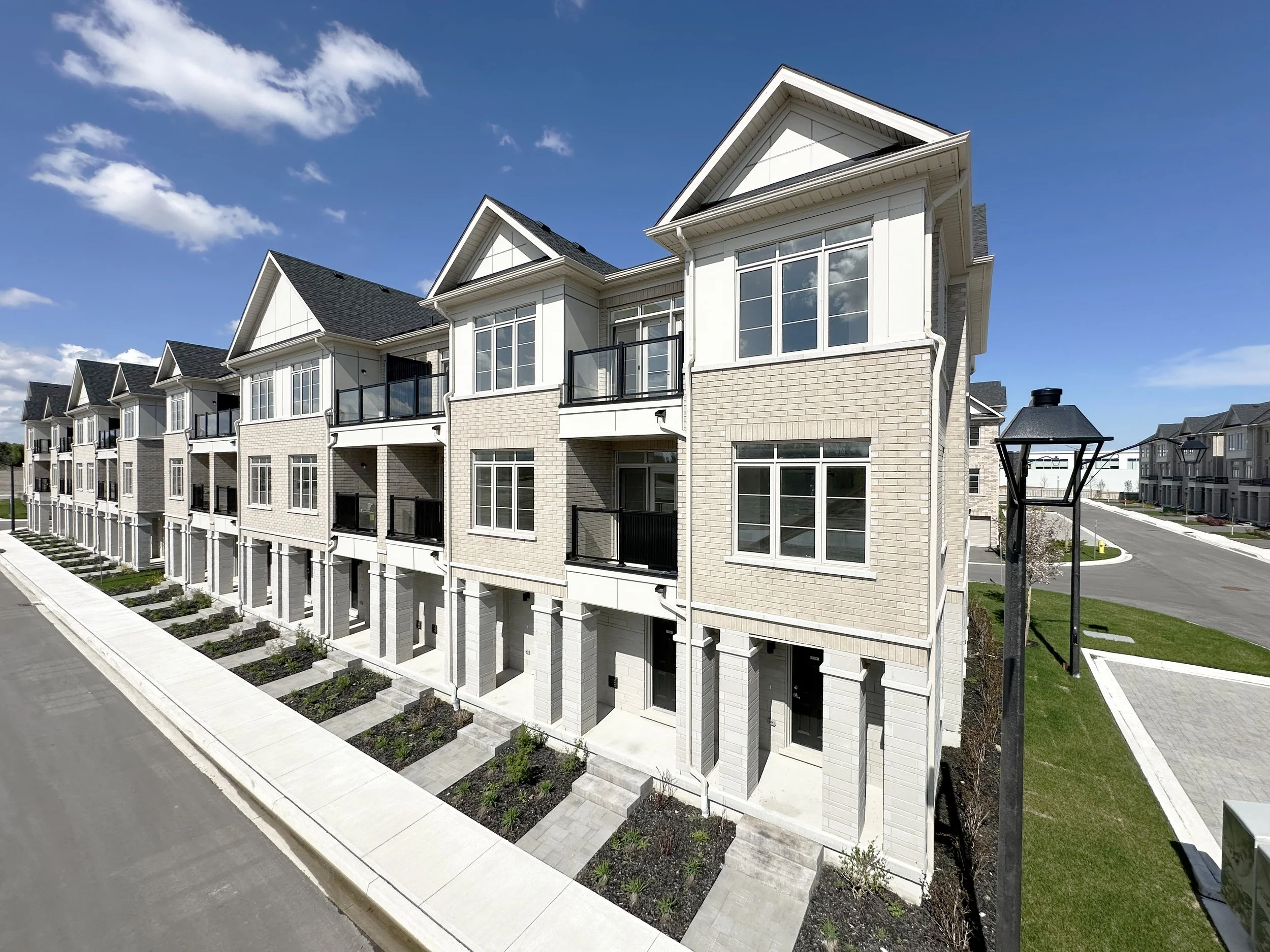 Row of modern multi-story townhouses with large windows, small balconies, brick and siding exteriors, under a partly cloudy blue sky.