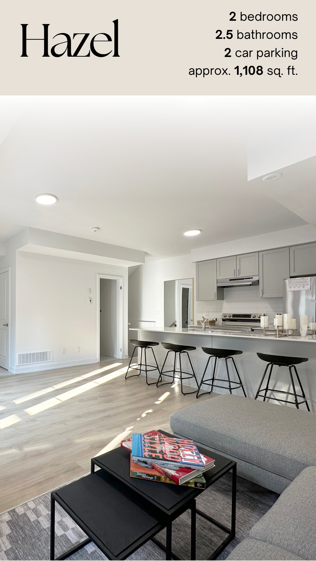 Modern living room and kitchen with white walls, gray cabinets, black bar stools, and sunlight streaming in.