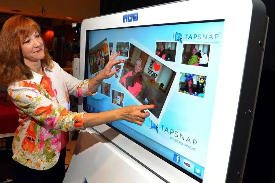 Woman using an interactive TapSnap photo booth touchscreen displaying a collage of event photos