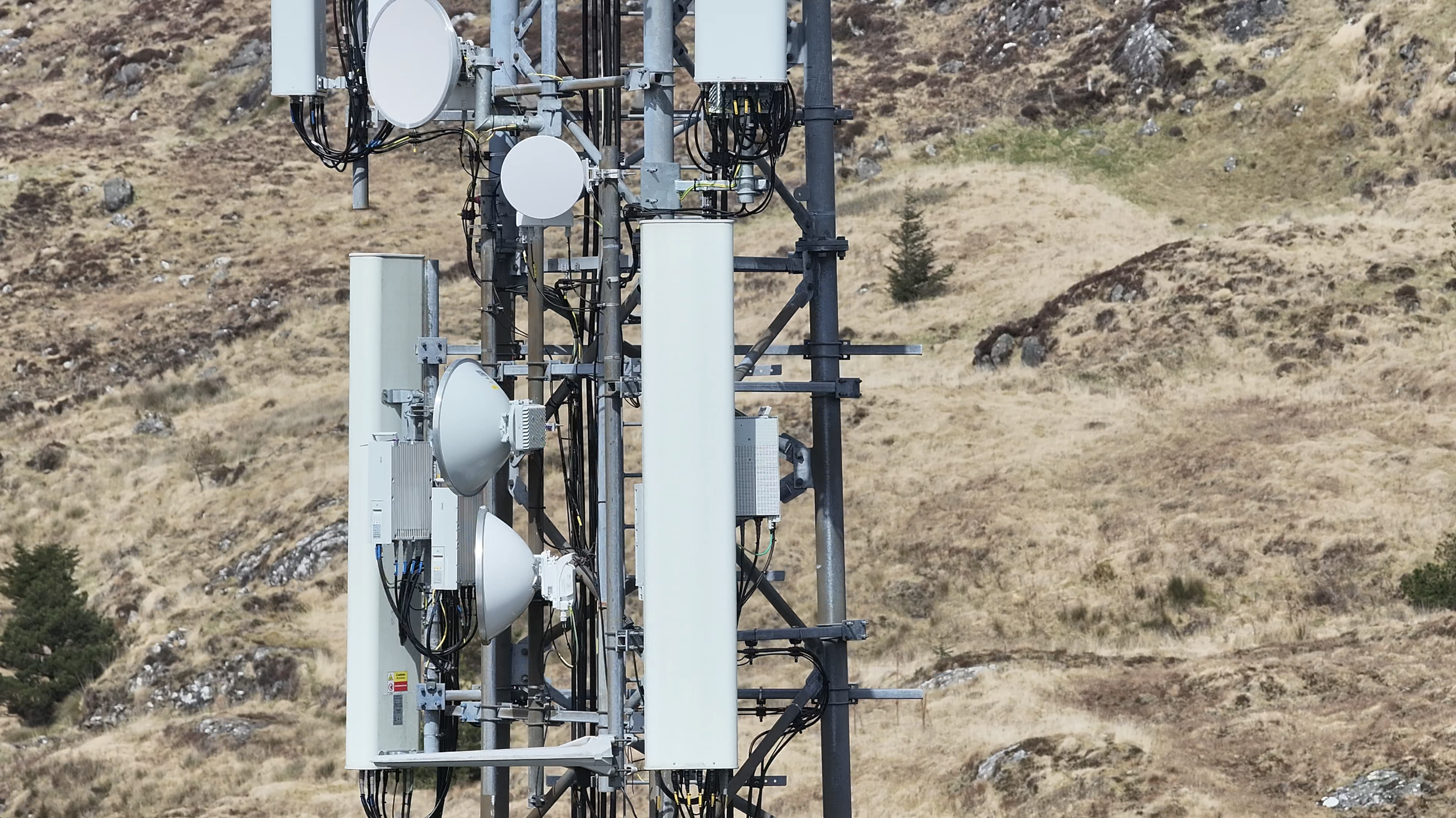 A cell tower in a grassy, hilly landscape with some small trees.