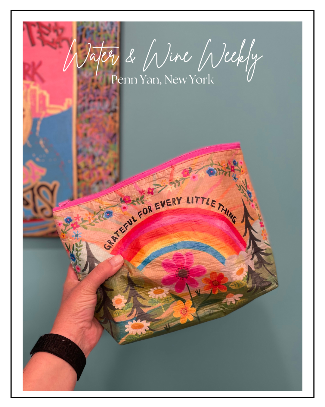 A hand holding a colorful zippered bag with a rainbow and floral design. The bag has the phrase 'Grateful for every little thing' written on it.