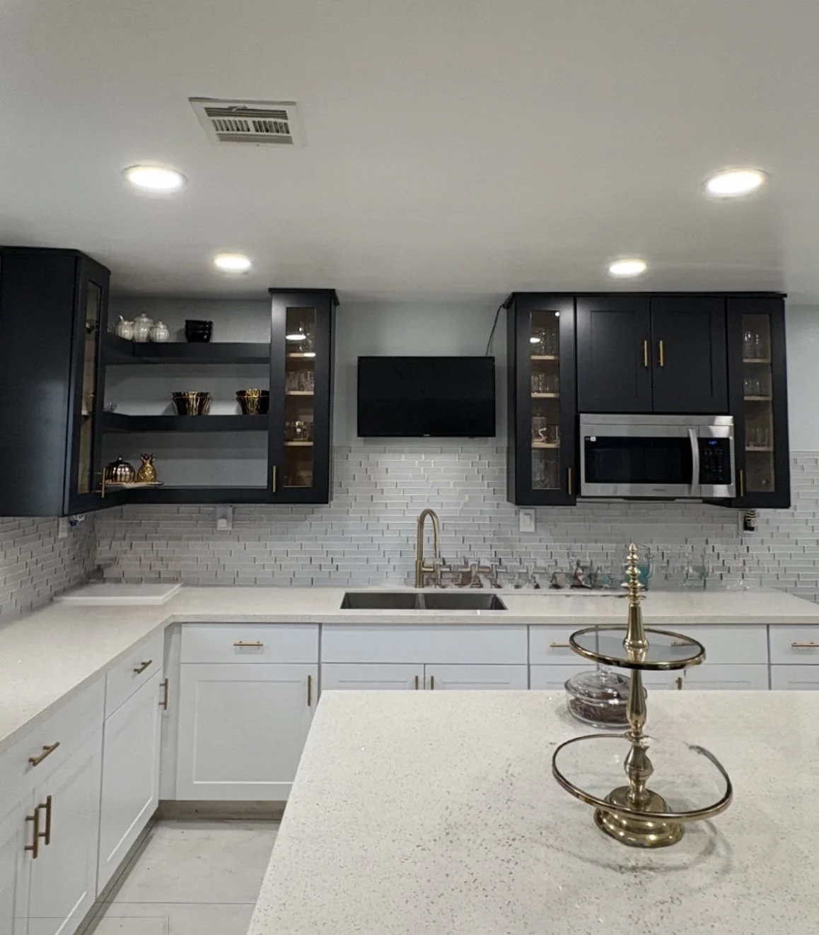 New remodeled kitchen with white countertops, black upper cabinets, and gray brick backsplash. 