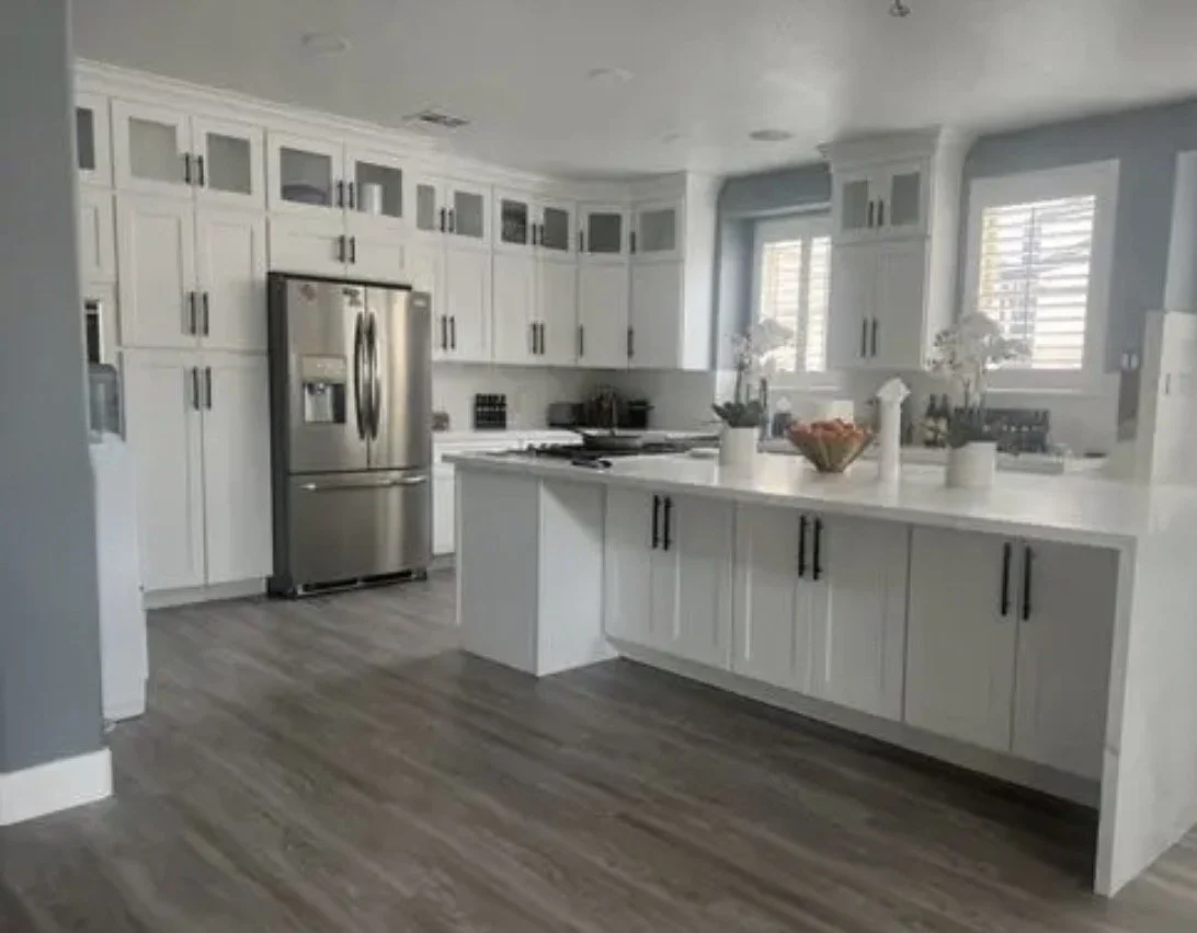 Modern white kitchen with stainless steel appliances, white cabinets, and a kitchen island with decorative vases and a bowl of fruit.