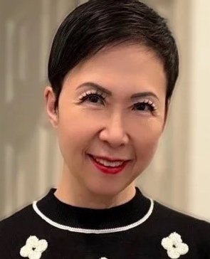 A woman with short black hair smiling, wearing a black top with white floral embroidery.