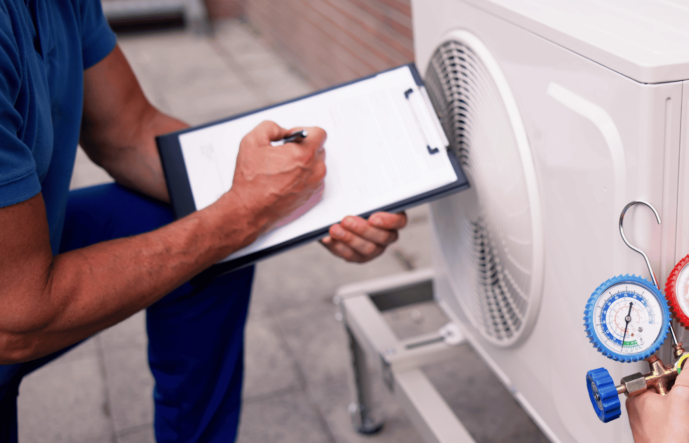 Technician recording data on a clipboard next to an air conditioning unit with gauges and refrigeration tools nearby.