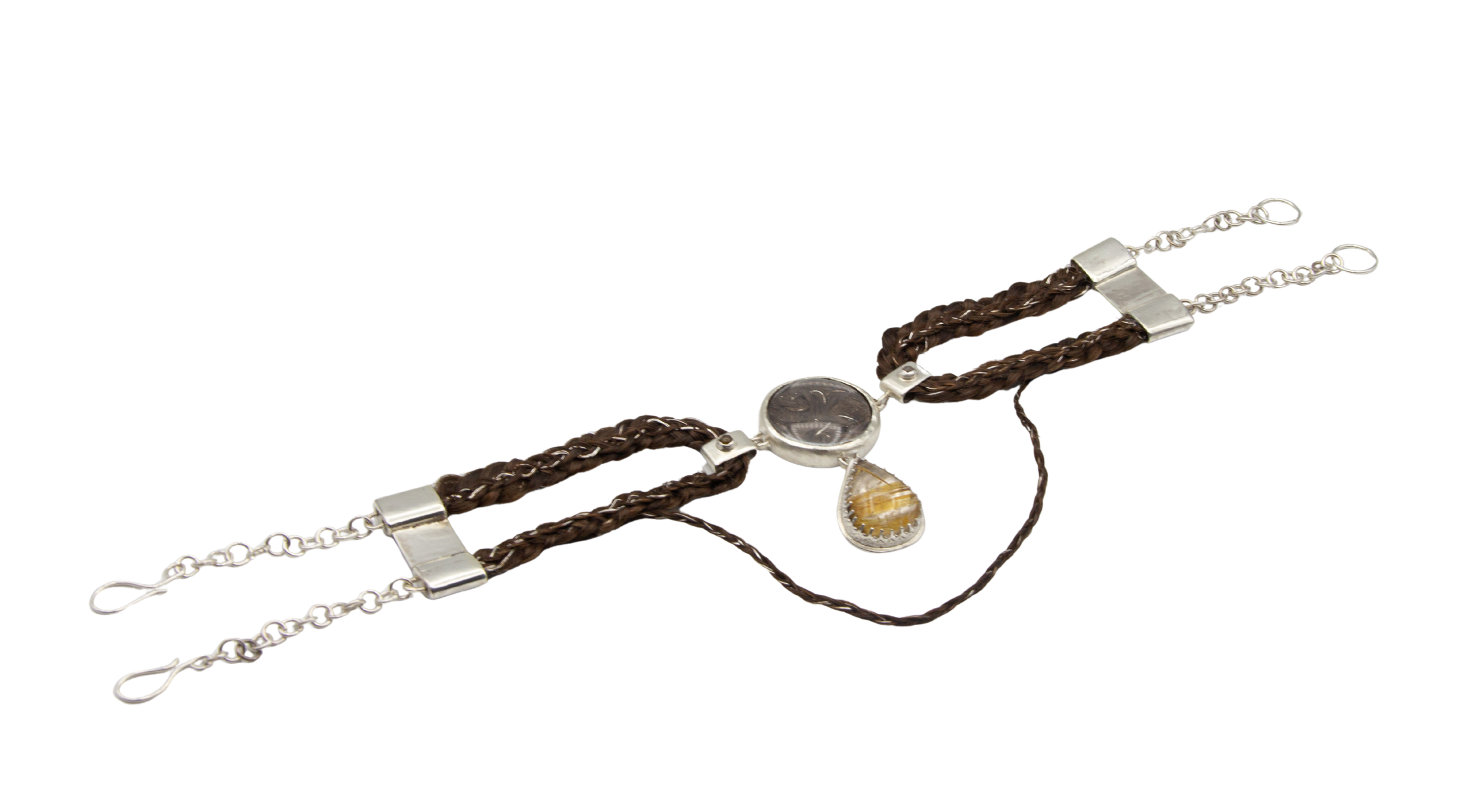 A collection of jewelry including two necklaces with brown braided leather chains and silver clasps, a silver chain bracelet, and a pendant necklace with a yellow gemstone in a silver setting.