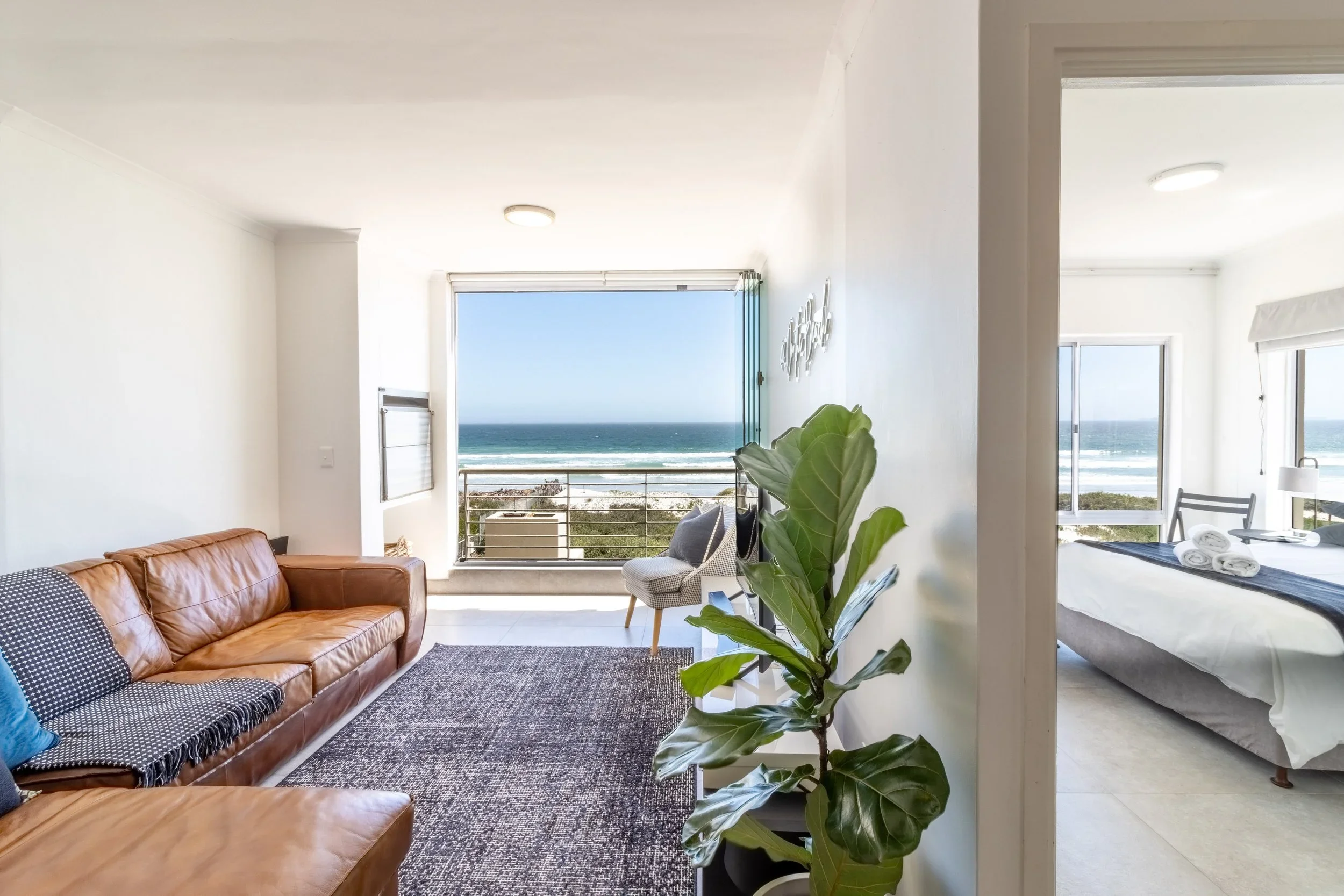 Living room with a leather sofa, a patterned rug, and large windows showing an ocean view.