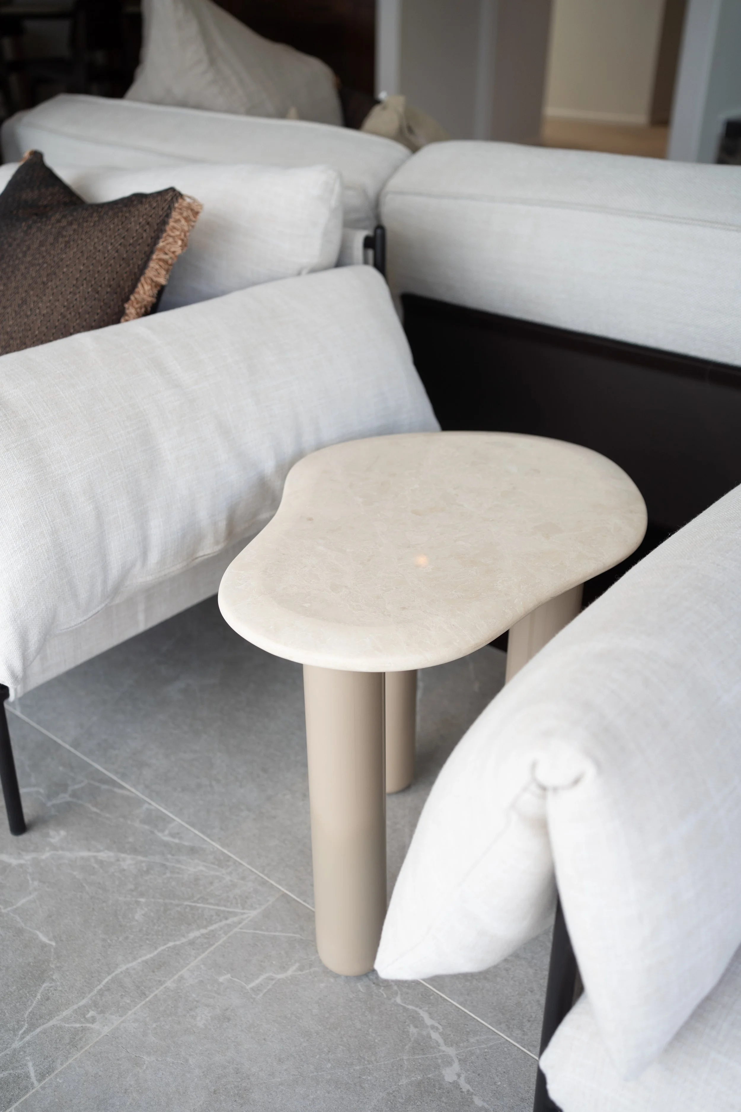 White upholstered sofas arranged around a small beige side table in a modern living room with gray tiled flooring.