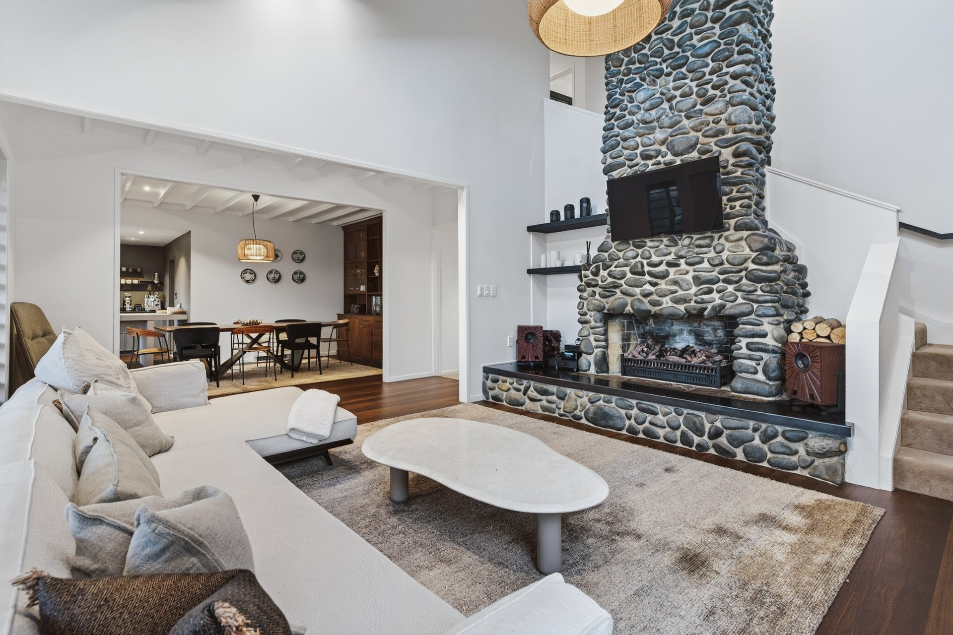 Living room with stone fireplace, white couch, and open view of dining area.