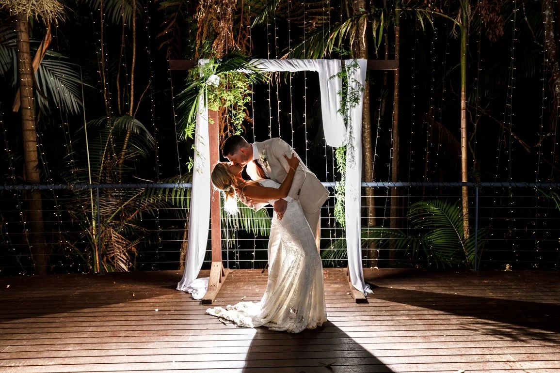 Couple embracing under a white wedding arch on the deck