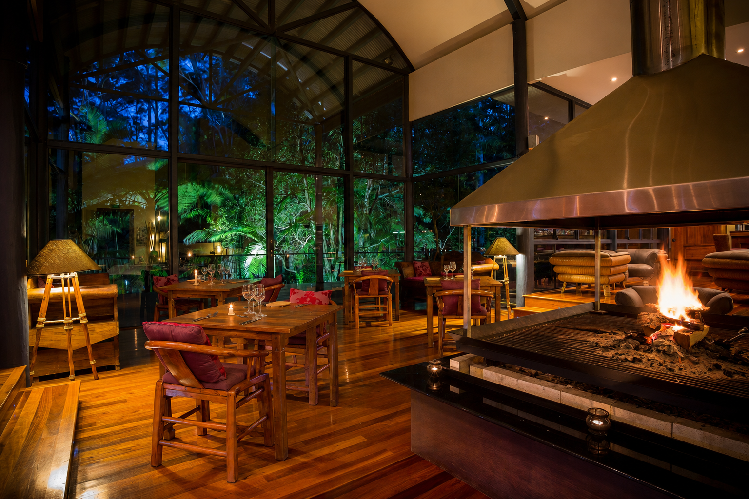 Restaurant interior with open fireplace and glass walls onto the floodlit rainforest