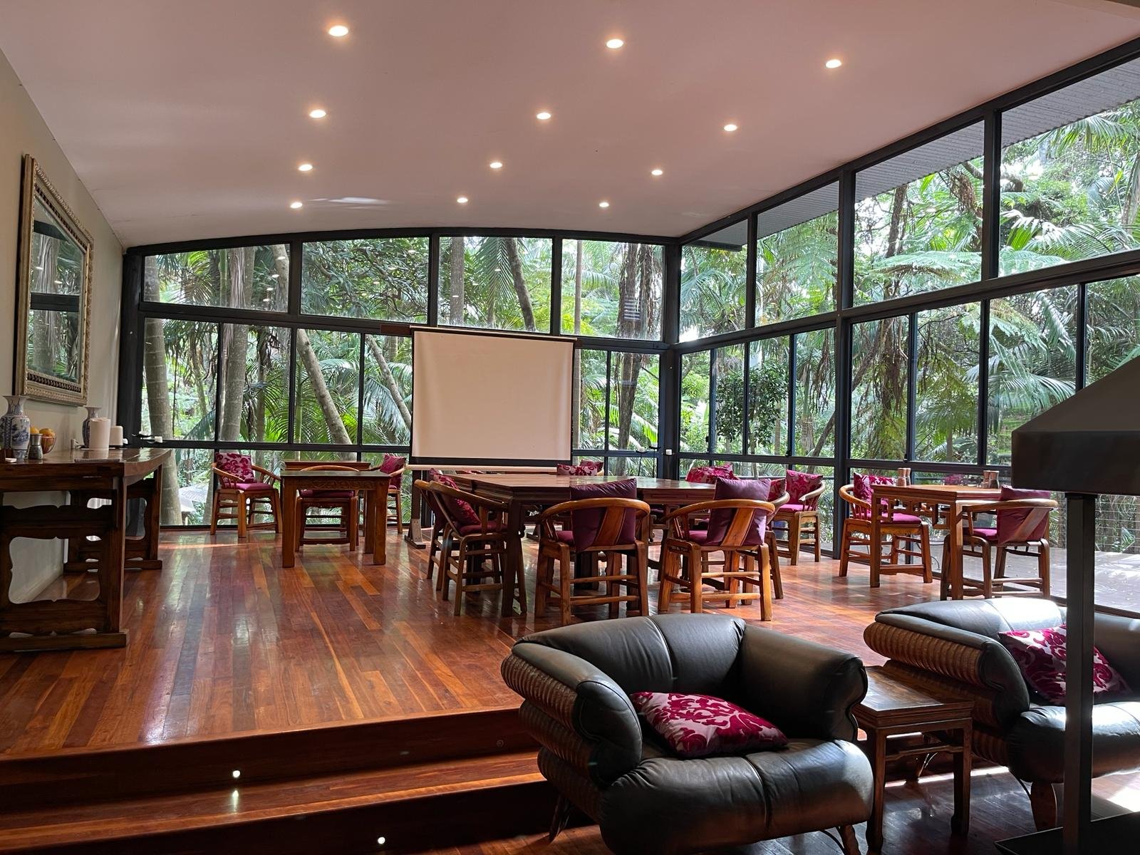Boardroom set up with projector screen and whiteboard, rainforest through the windows