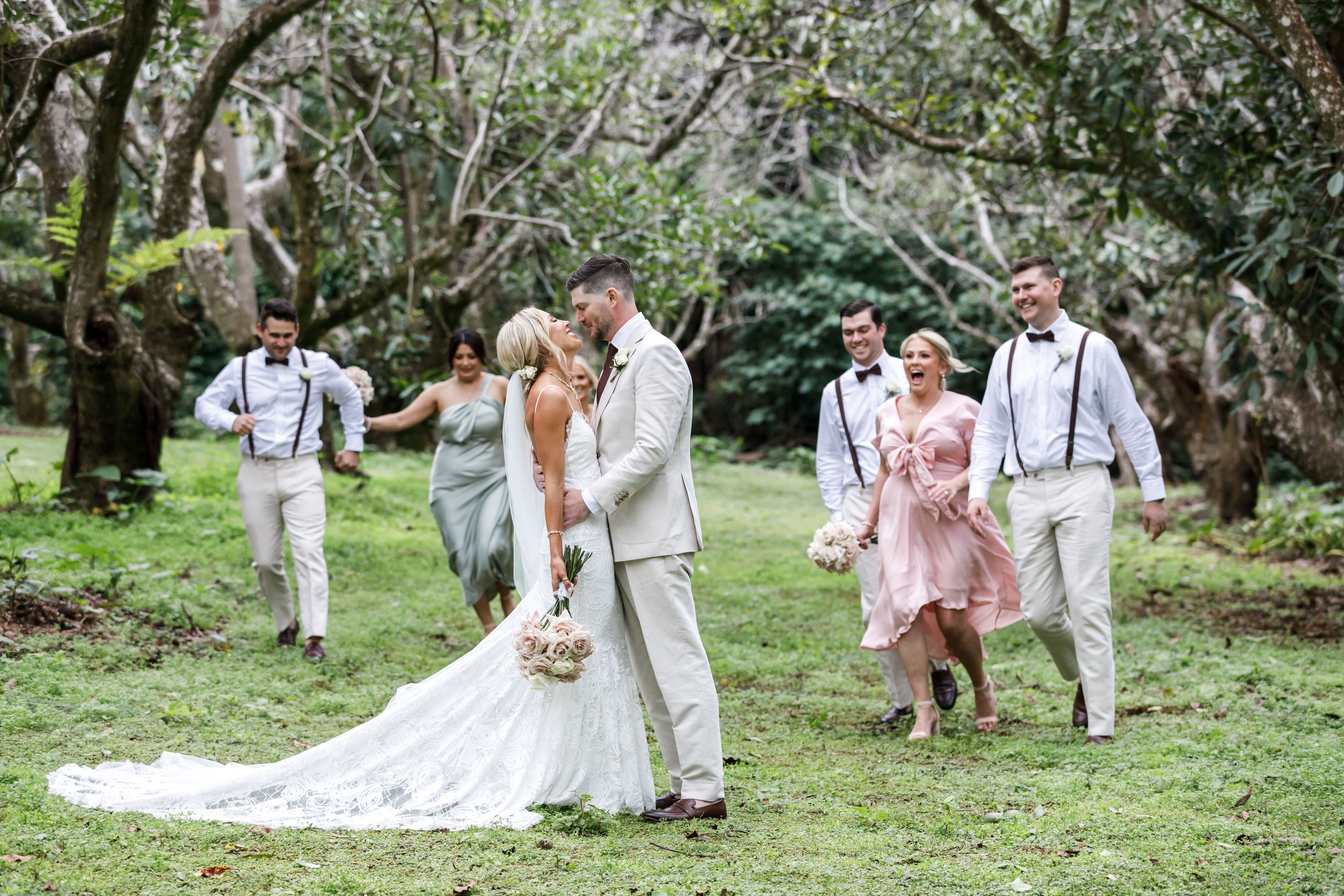 Newlyweds with bridesmaids on the lawn, rainforest behind