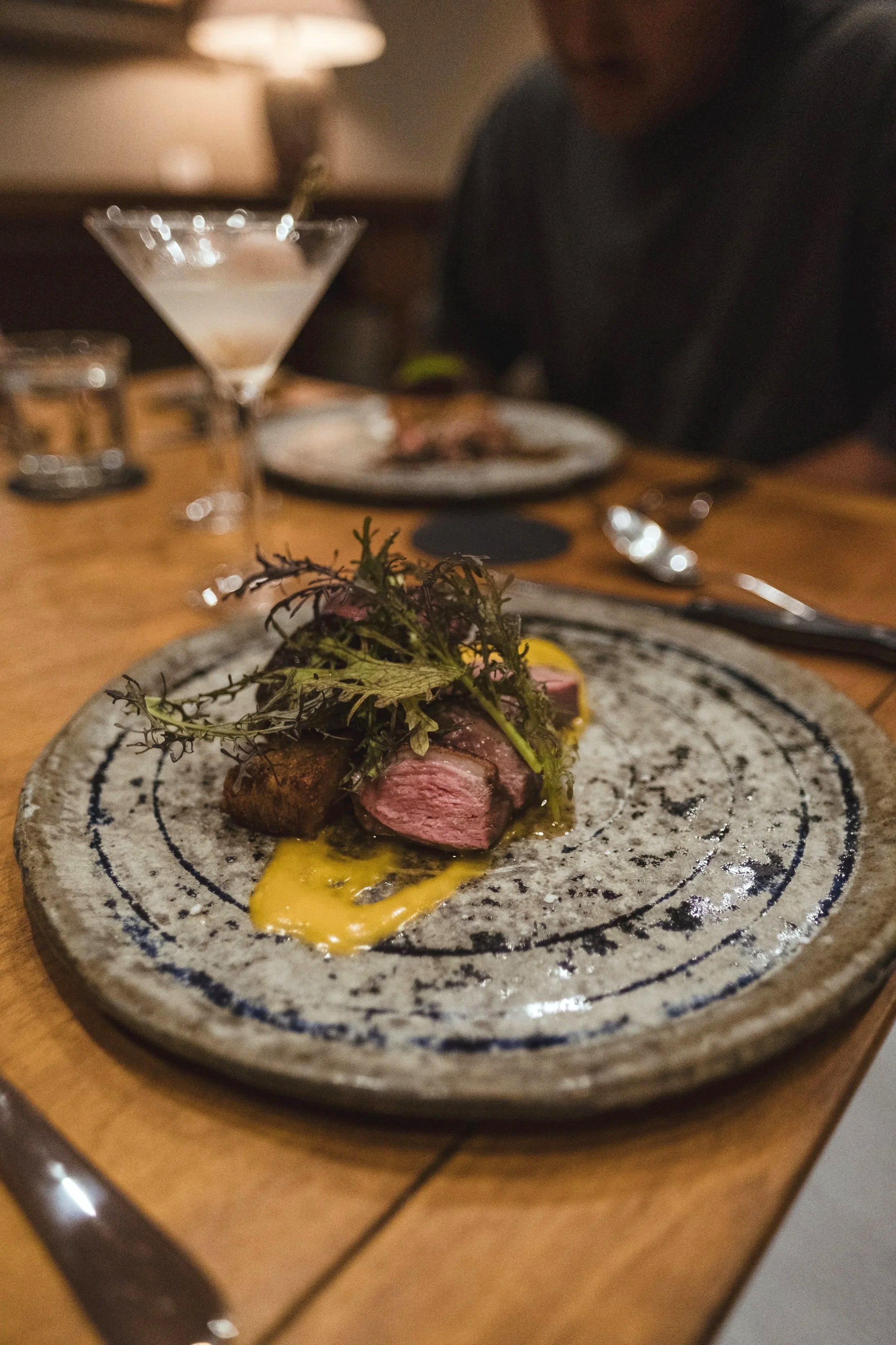Sliced beef with charred greens and mustard emulsion on a speckled plate