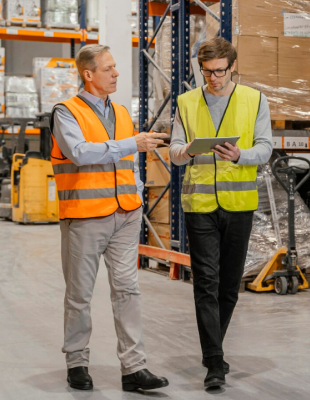 Two men in safety vests reviewing documents in a warehouse.