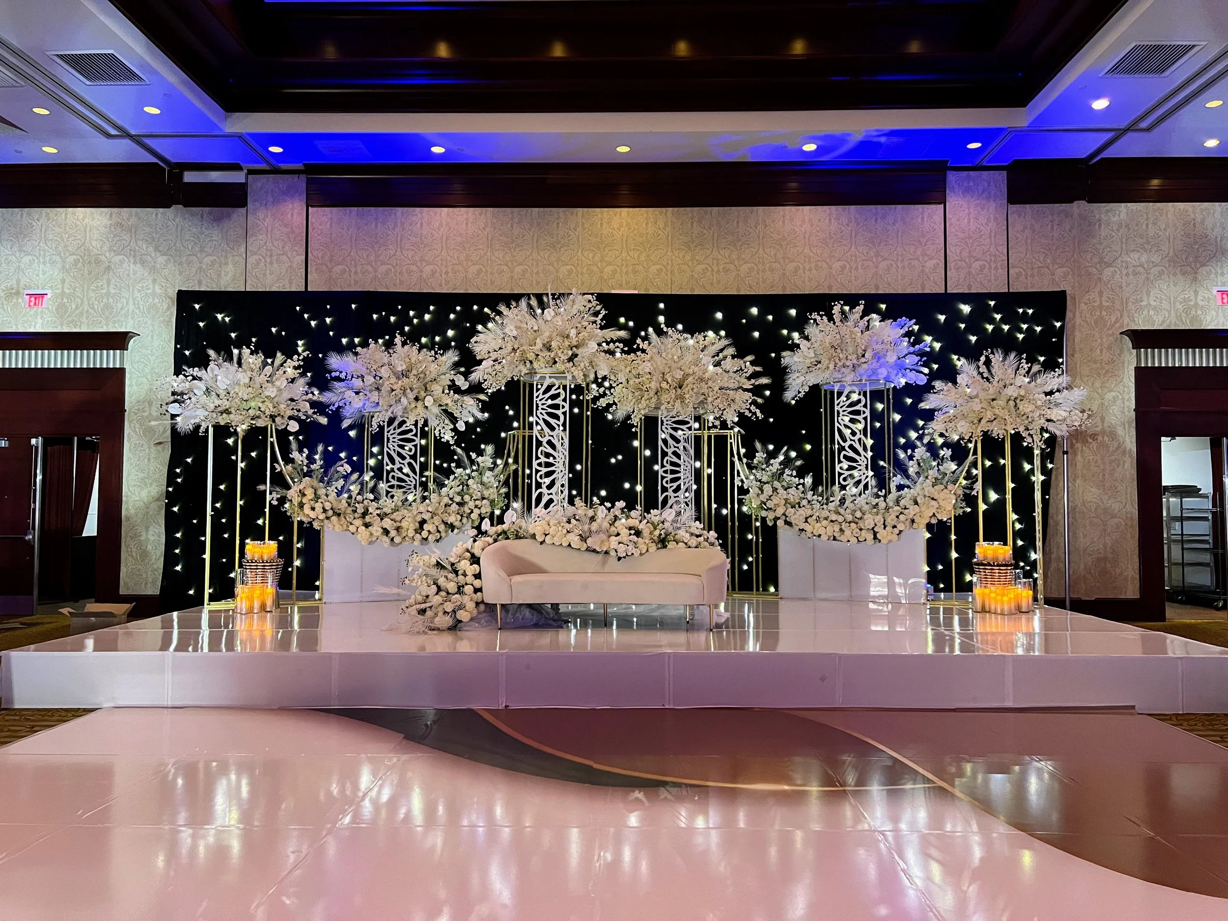Elegant event space decorated with white floral arrangements and soft lighting, with a stage area prepared for a wedding or special celebration.
