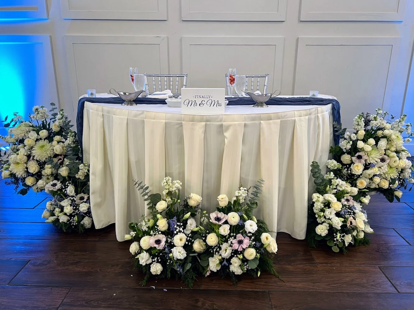 Wedding reception table with floral arrangements, a sign that says 'Finally Mr. & Mrs.', and two champagne glasses with pink drinks.