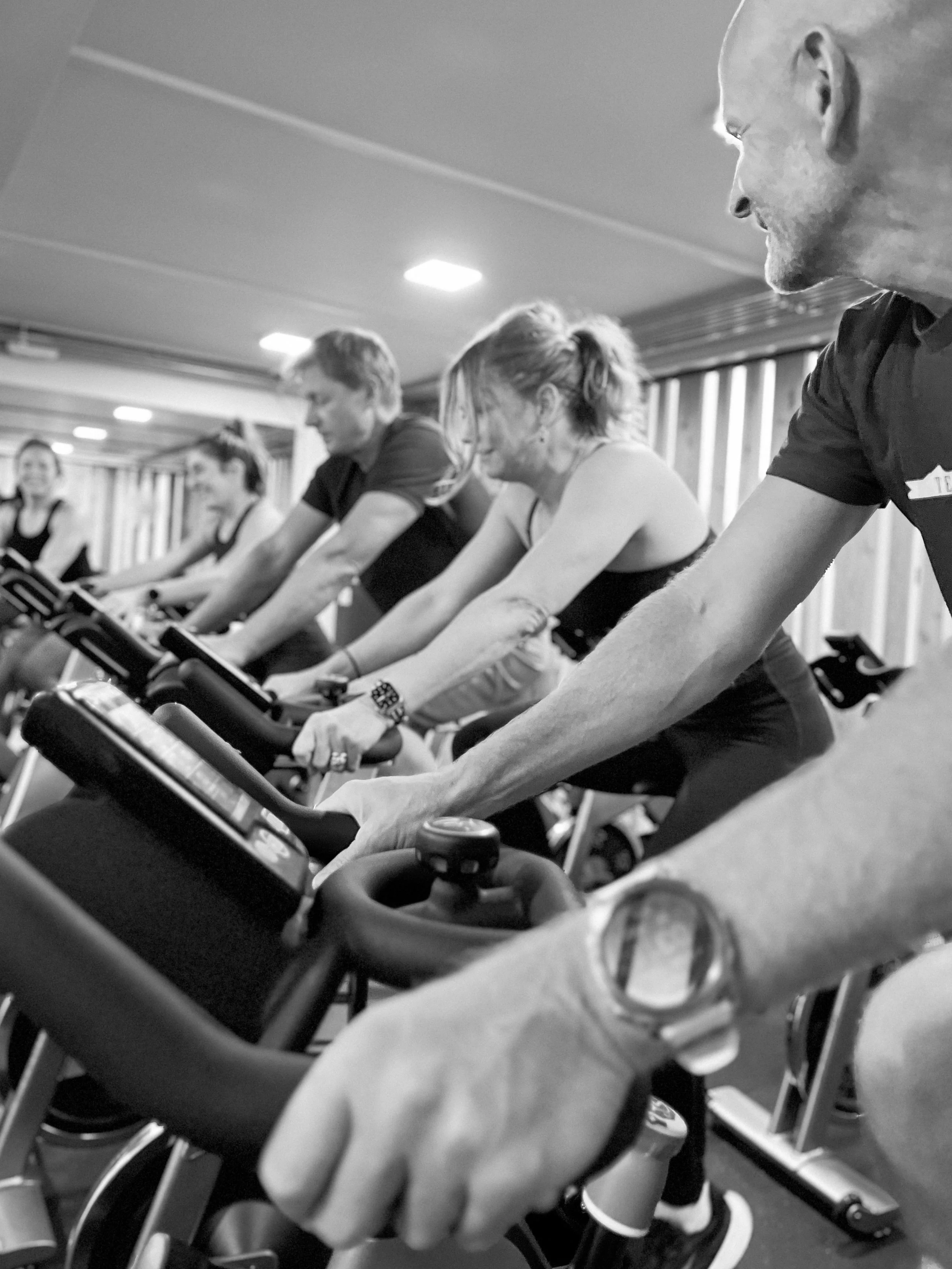Group of people exercising on stationary bikes in a fitness class, smiling and focused.