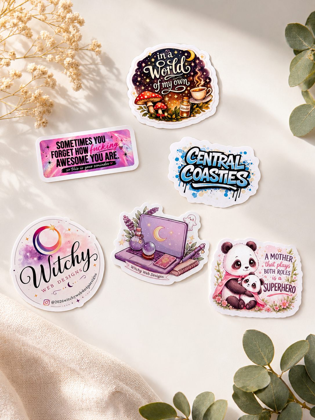 Collection of six stickers with various designs and messages including a witch-themed sticker, motivational quote, graffiti style logo, a mystical laptop design, panda illustration, and a phrase about motherhood, arranged on a white surface with drie