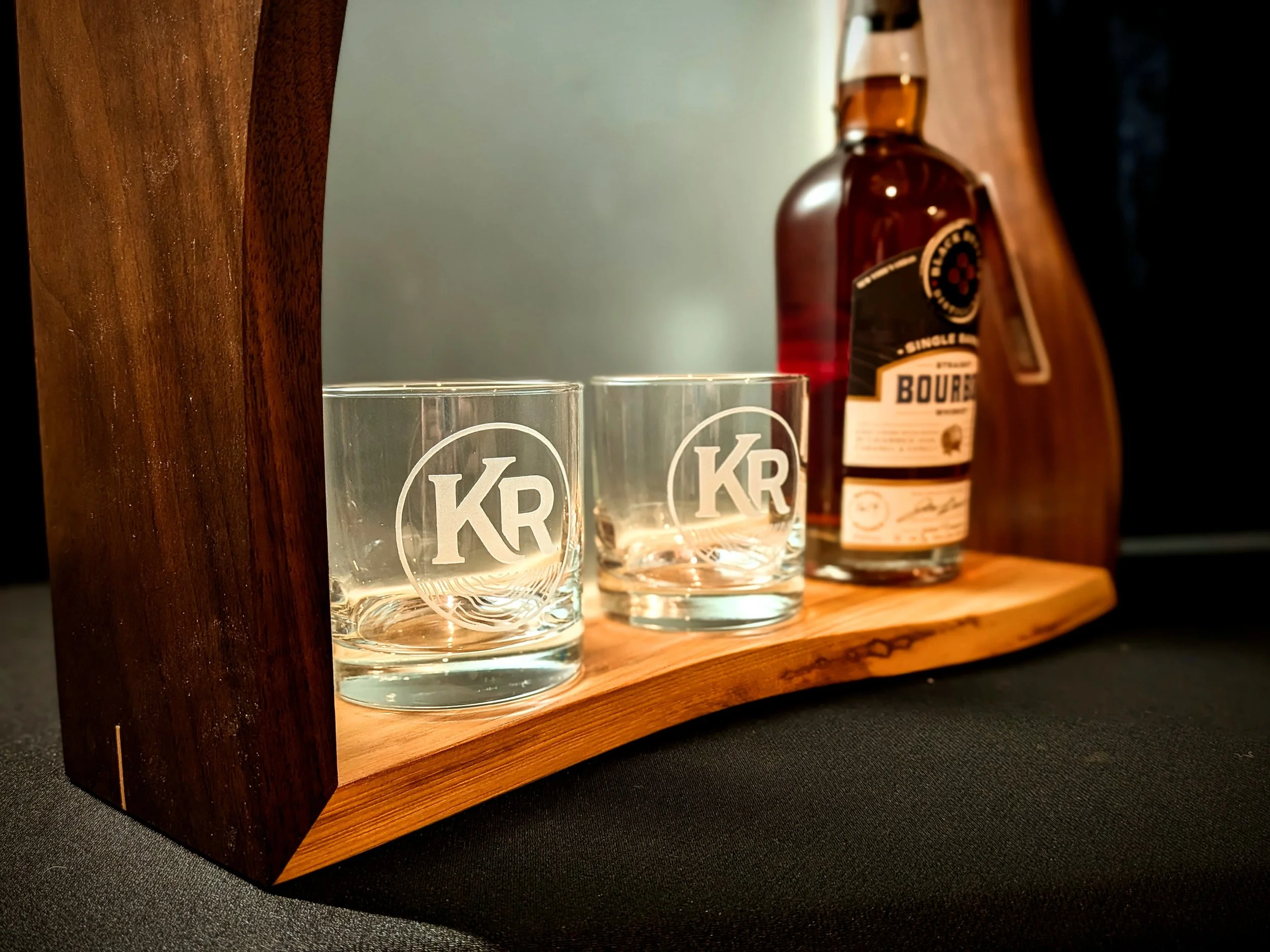Wooden bar stand holding two glasses with initials "KR" and a bottle of liquor.