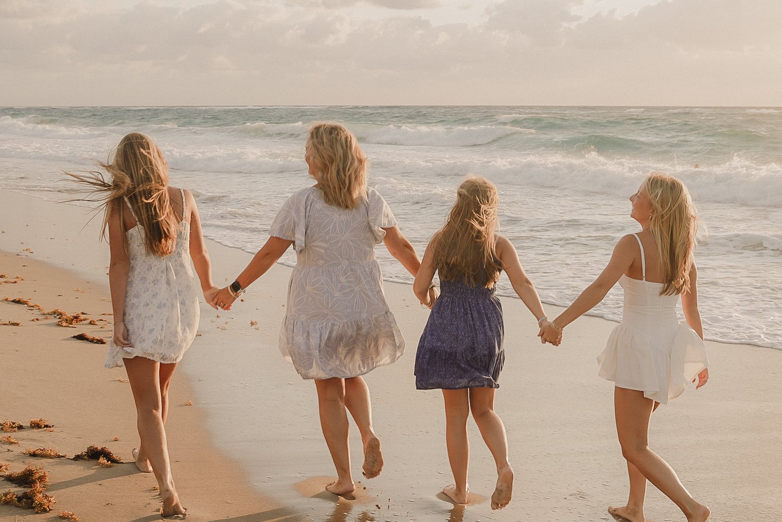 Honey+Haze Photography. Four women walking hand in hand on the beach during sunset, with waves in the background.