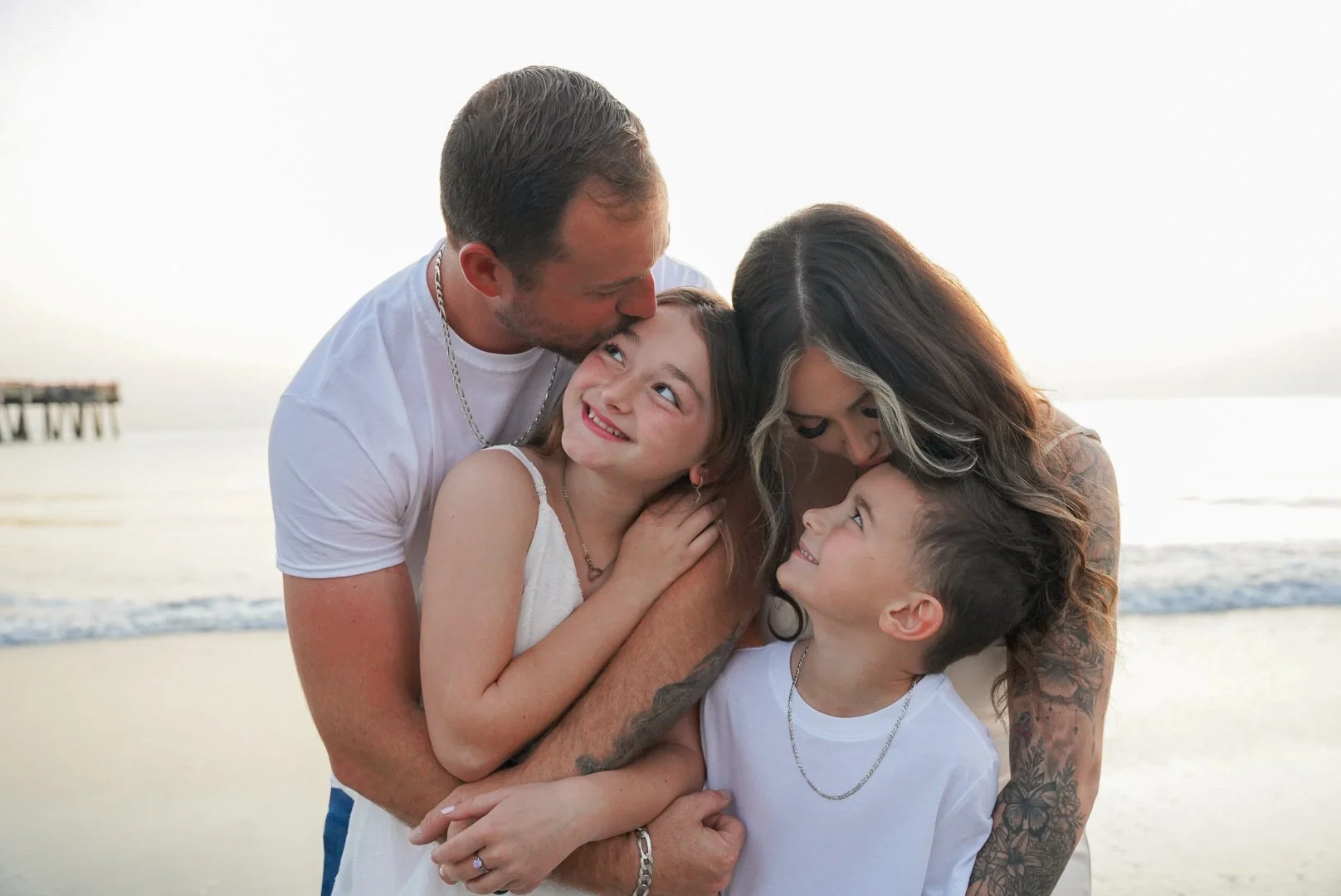 Honey+Haze Photography. A family of four on a beach at sunset, embracing and smiling at each other.