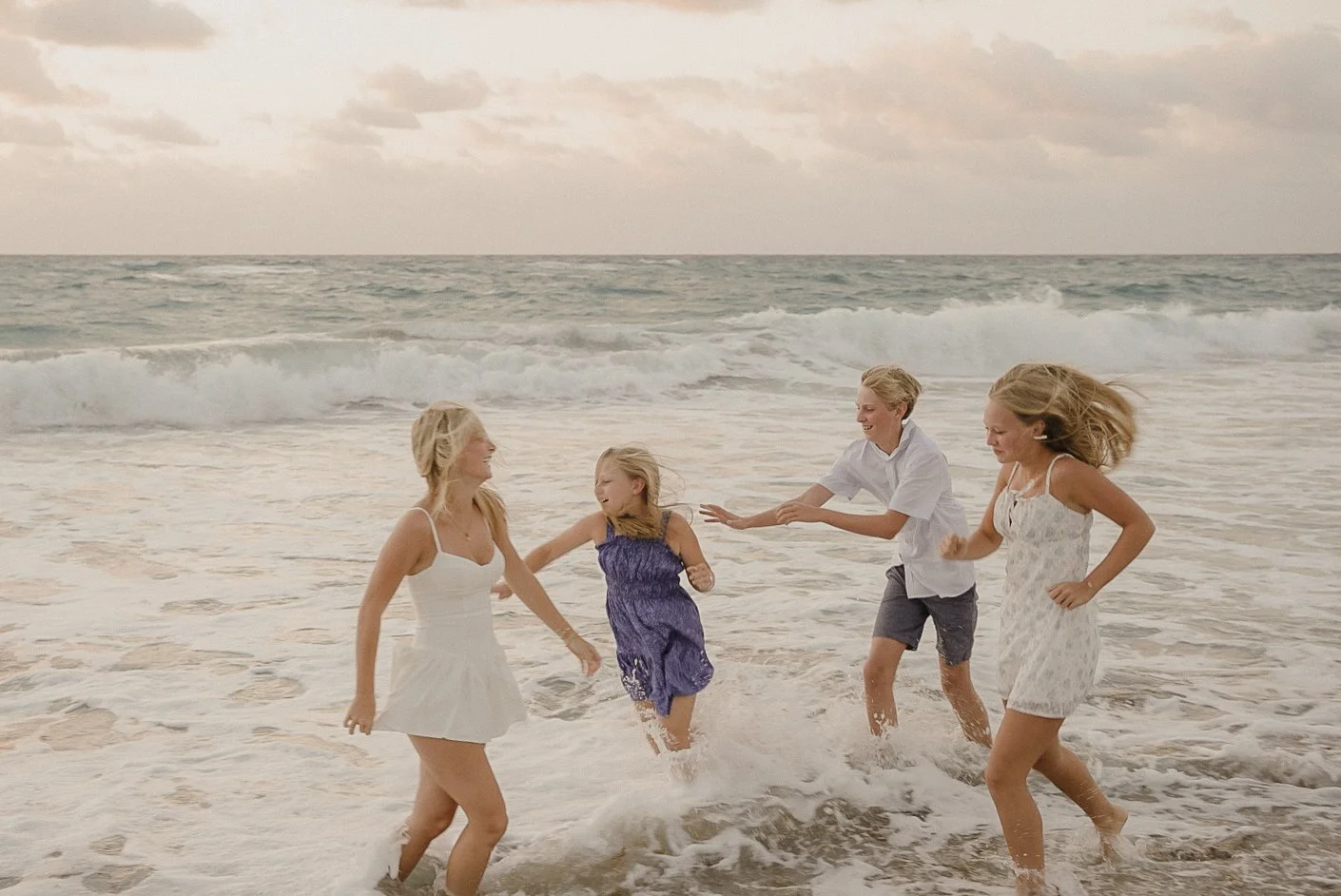 Honey+Haze Photography. Four children playing and running in the ocean waves at the beach during sunset.