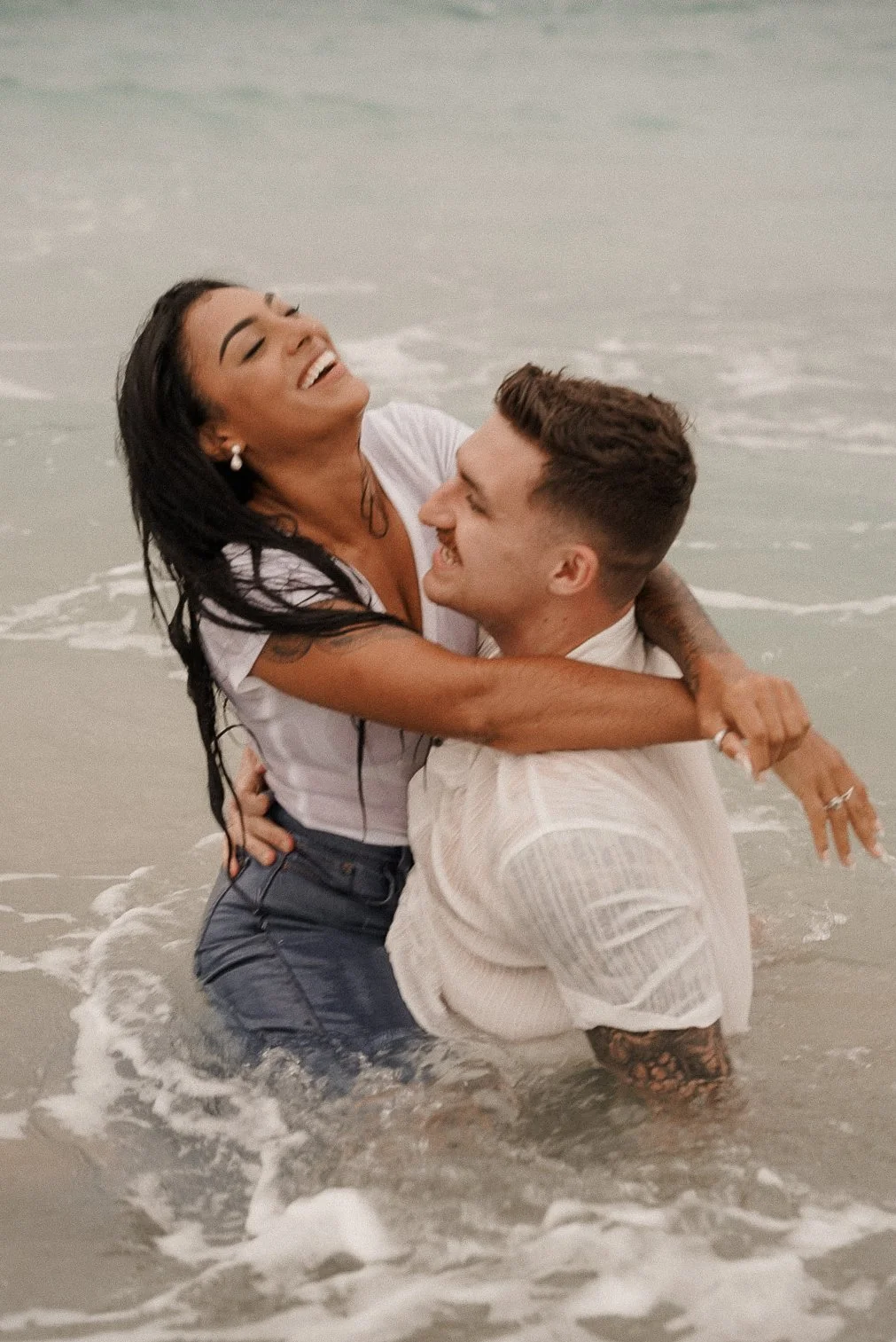 Honey+Haze Photography. A happy couple playing and embracing in the shallow ocean water at the beach.