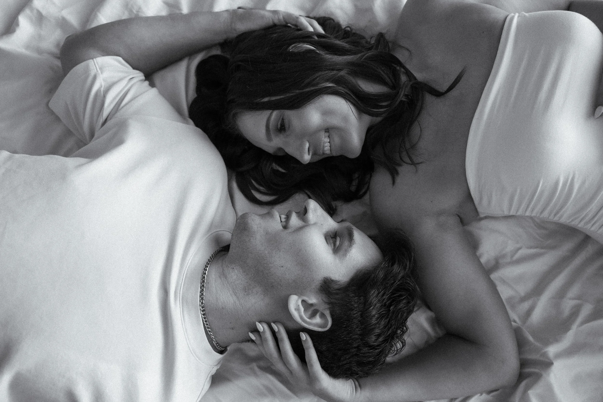 Honey+Haze Photography. A woman and a man lying on a bed close to each other, smiling and looking into each other's eyes.