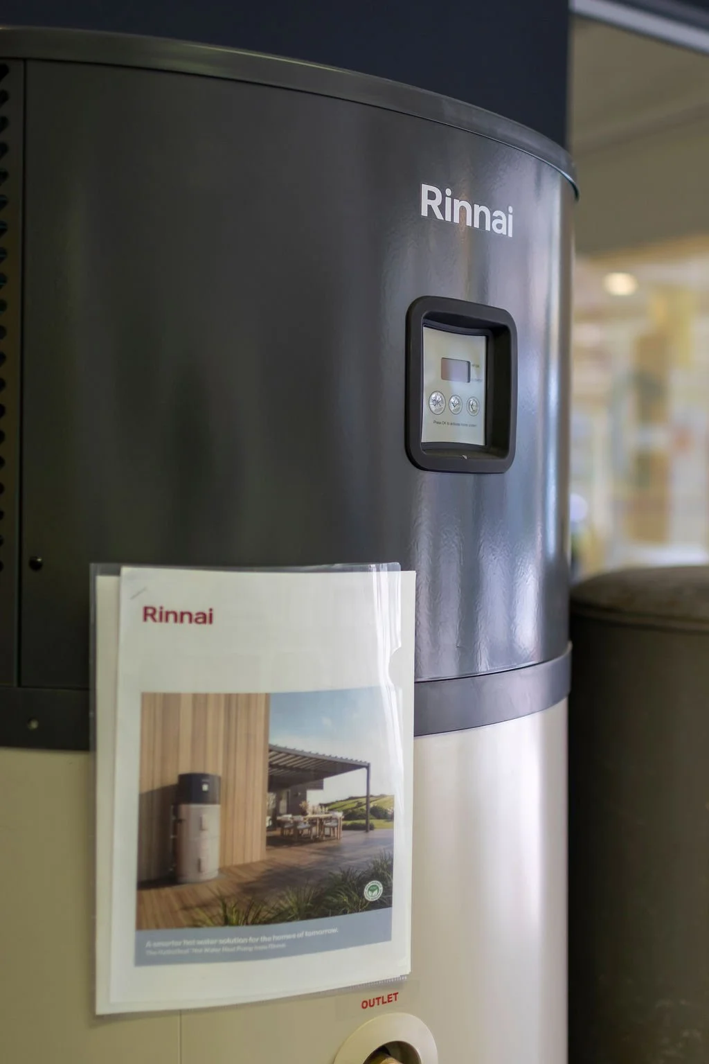 A Rinnai water heater with digital display and control panel, located indoors next to a brochure.