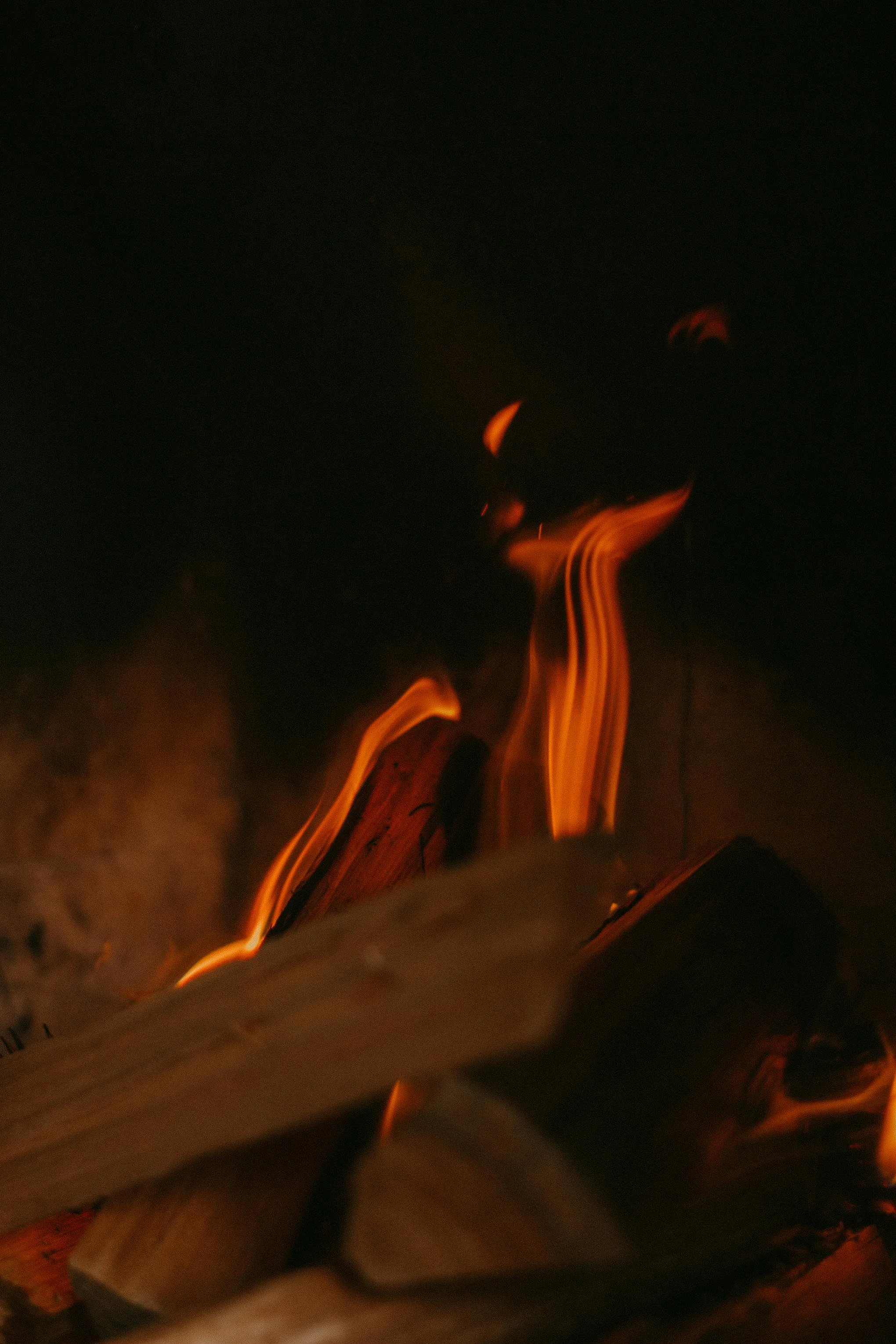 A campfire with glowing orange flames and burning logs in darkness.