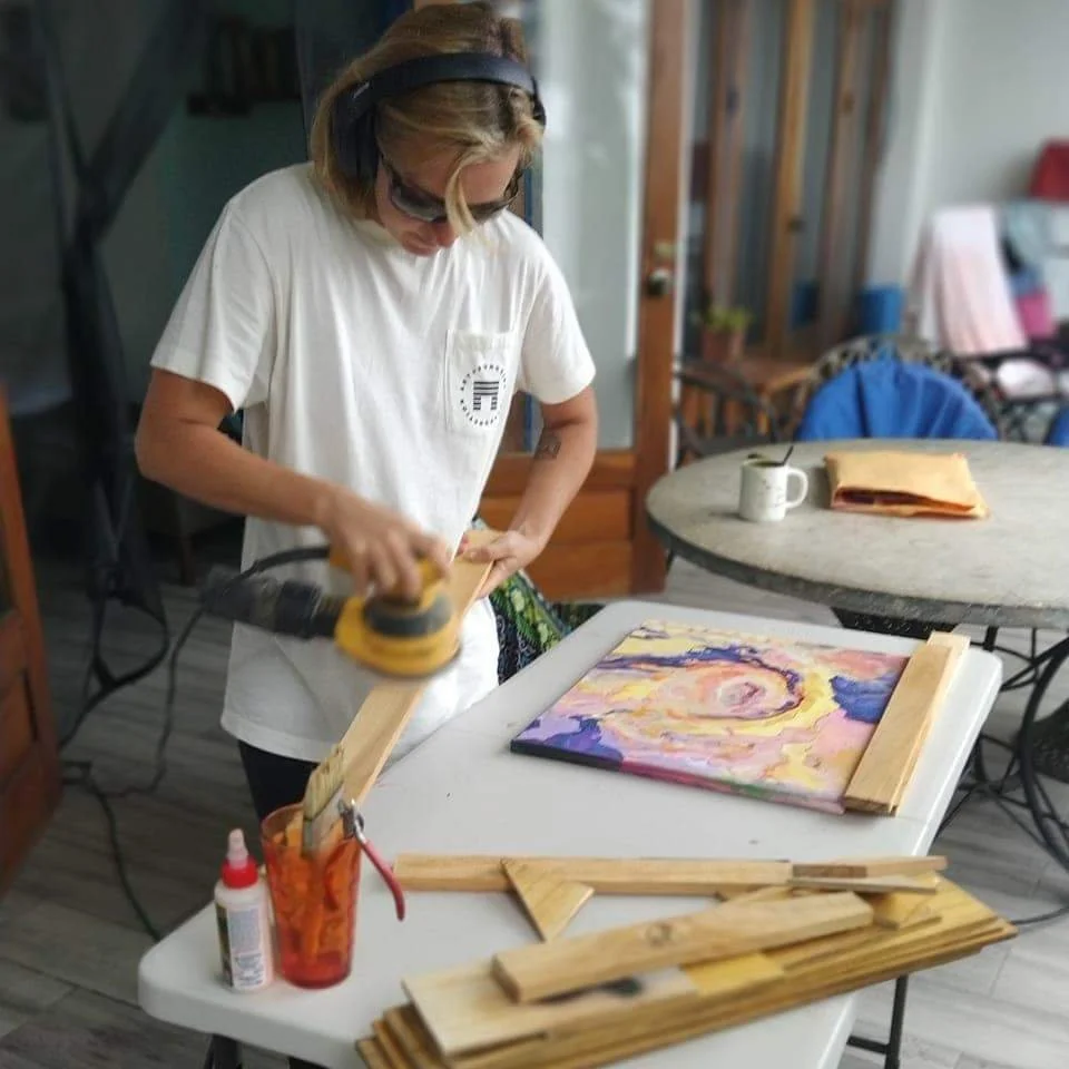 Person sanding a framed artwork at a table in a creative space.