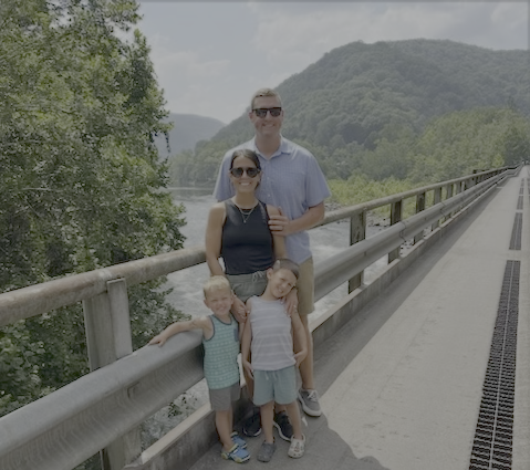 A family of four standing on a bridge with mountains and a river in the background.