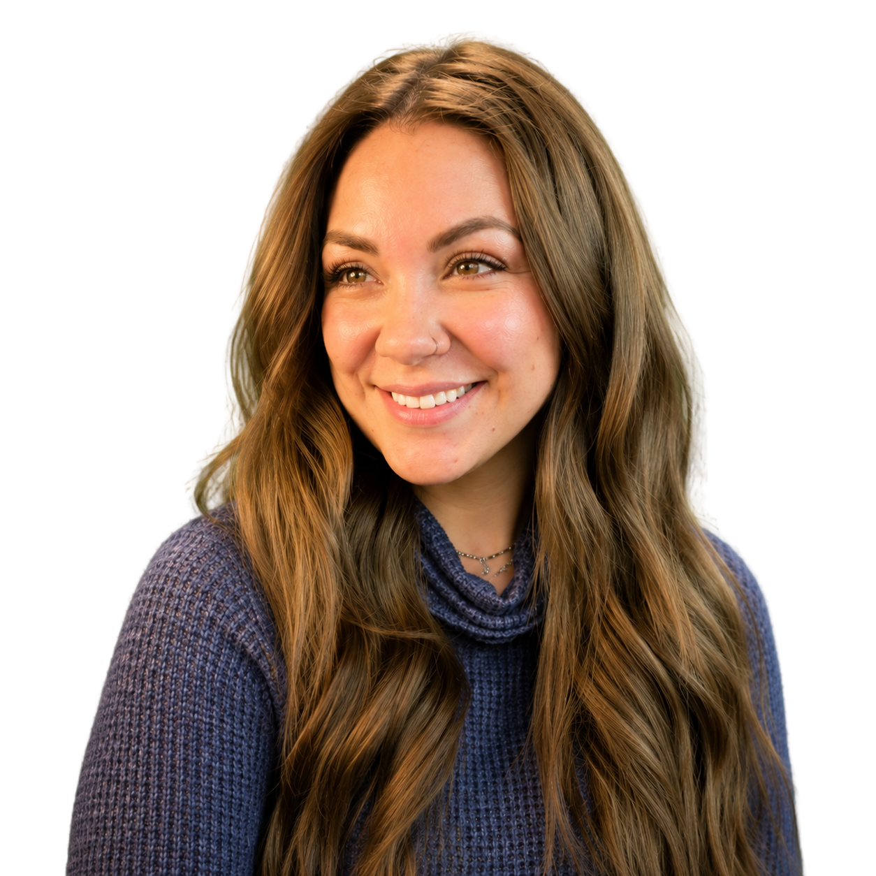 Young woman with long wavy brown hair smiling wearing a blue knit sweater and layered necklaces, looking to the side.