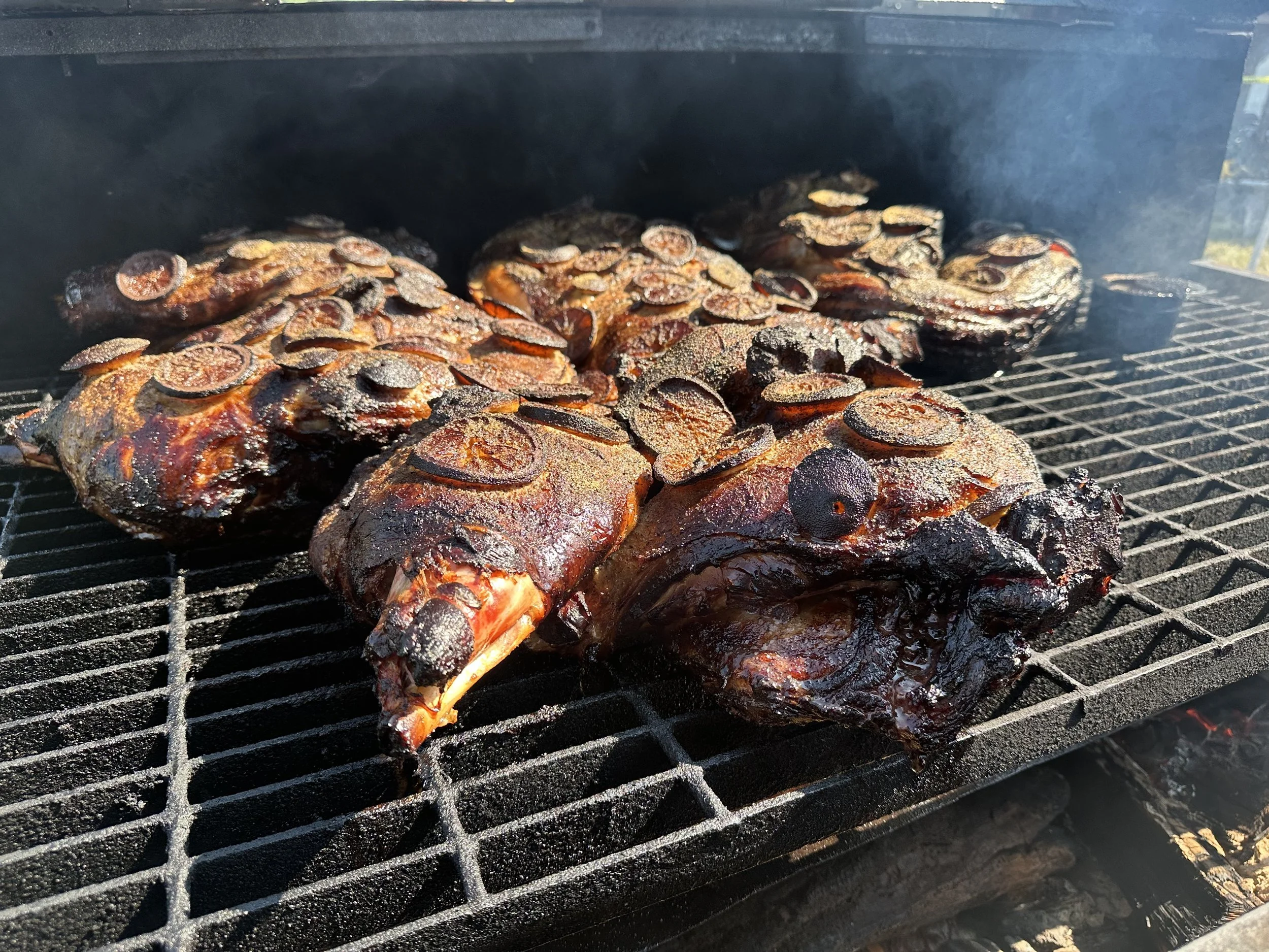 Barbecue grill with multiple racks of meat cooking, with a close-up view of the meats with charred edges.
