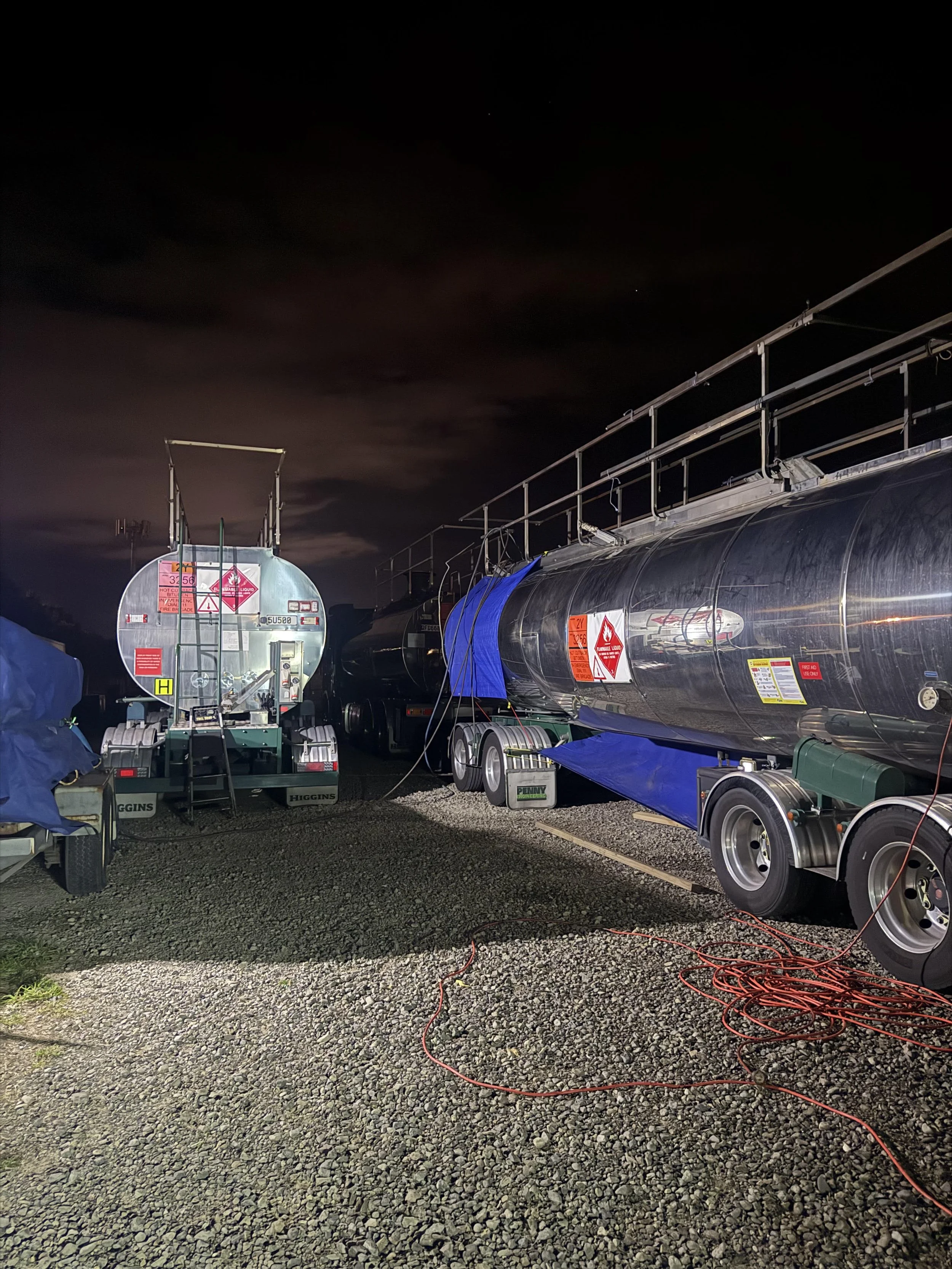 Nighttime scene with two bitumen tank trucks.