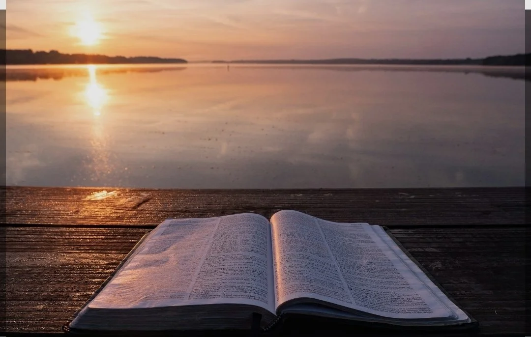 Open book on a wooden dock at sunset with a calm lake in the background.