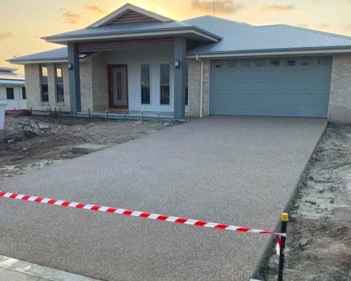 Newly constructed modern house with a driveway, front porch, and a garage, surrounded by construction site with some debris and a barrier at the front.