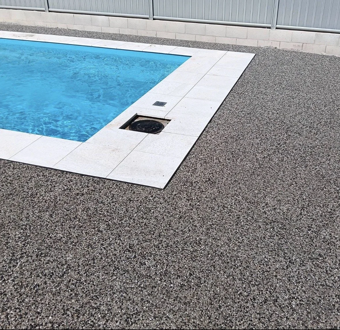 Close-up of a backyard swimming pool with blue water, white tile border, and textured gray concrete surrounding it.