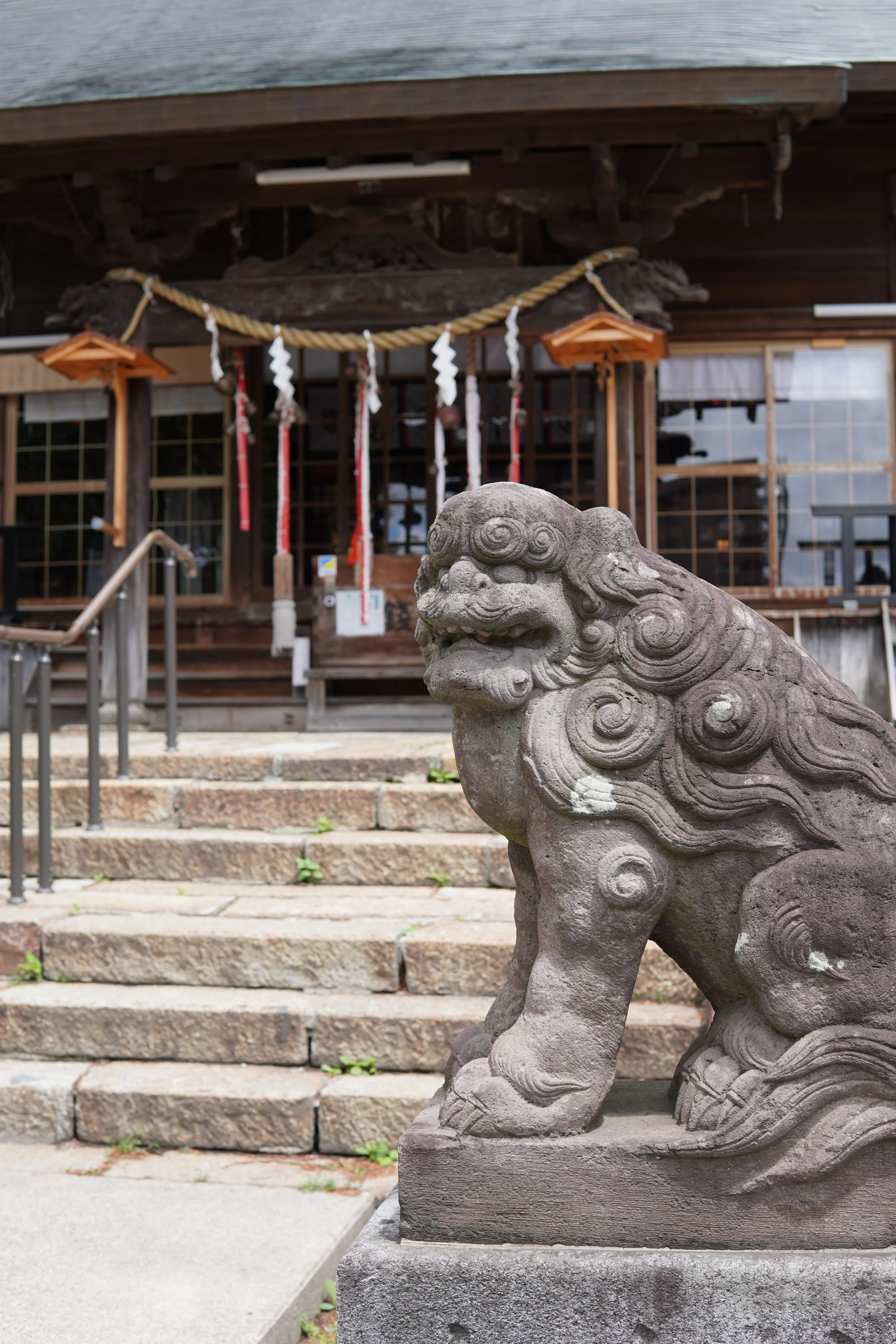 神社の入り口に置かれた狛犬の像と、階段の上に建つ木造の神殿