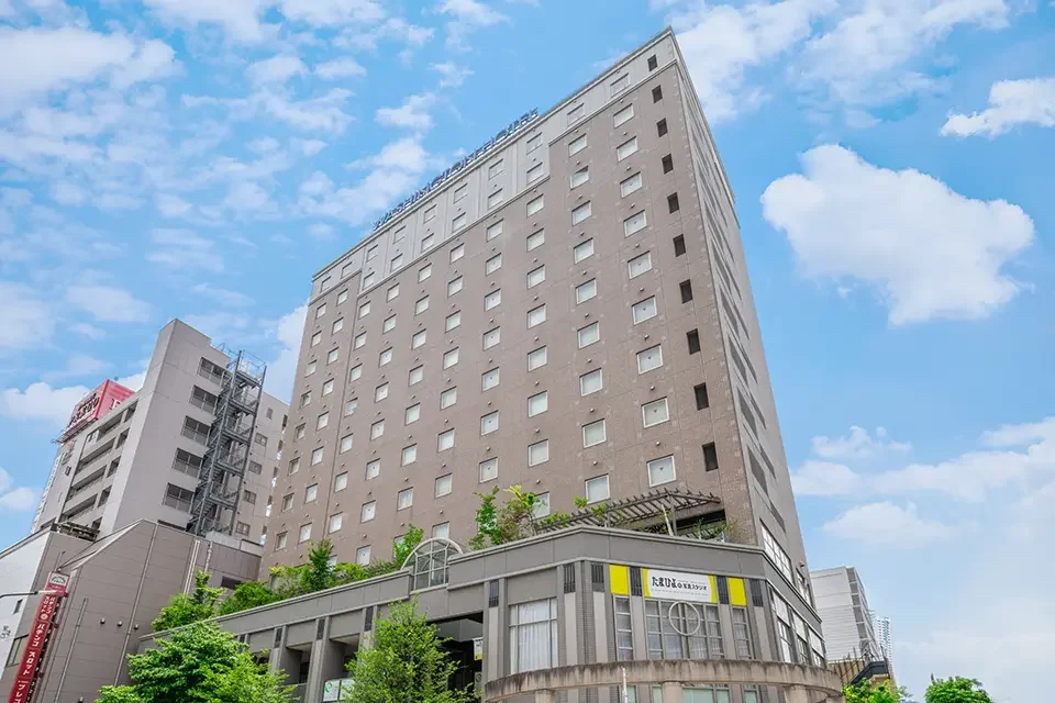 Tall beige hotel building with multiple windows under a blue sky with scattered clouds.