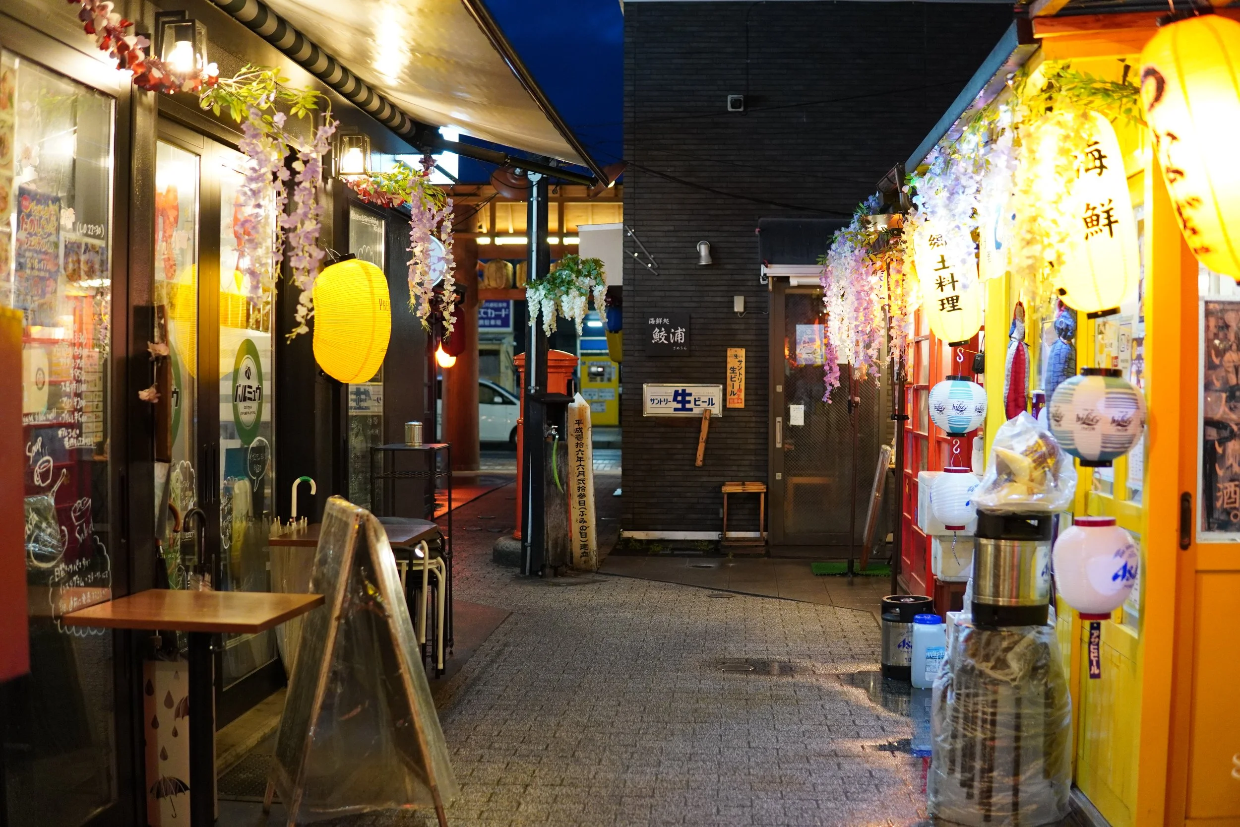 夜の飲食店街の通りで、提灯や彩lenれ飾りが並び、暖かい照明が灯っている。