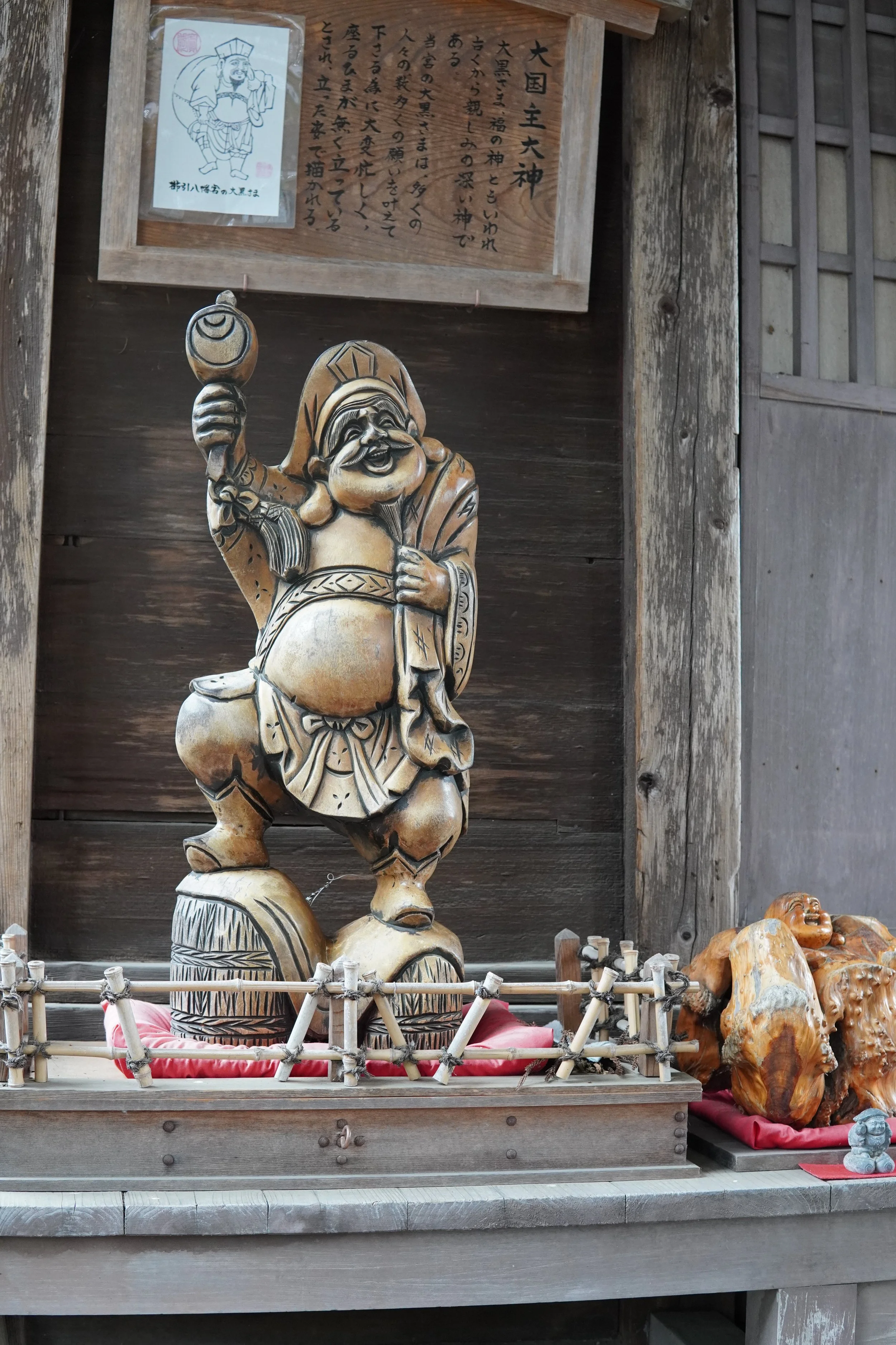 お金を持ち上げて笑っている大黒天の木製の像が祭られている、木の背景と囲いのある場所