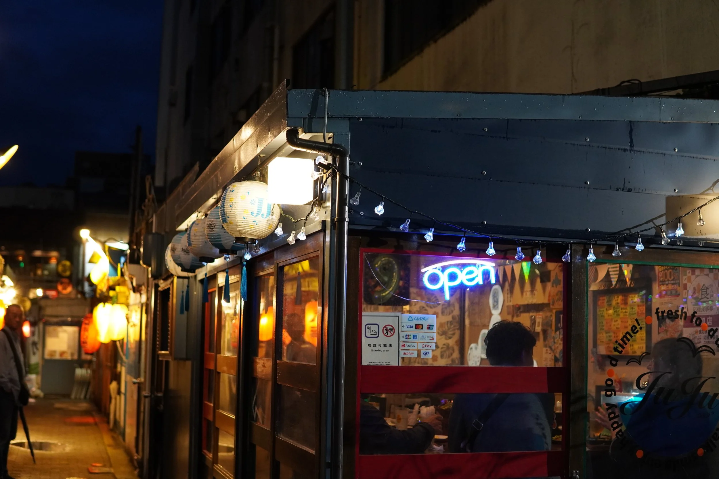 夜の屋台。ランタンとネオンサインの看板が見える。