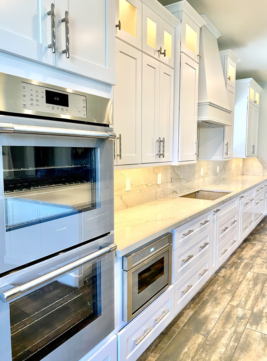 Modern kitchen with white cabinets, stainless steel appliances, marble countertops, and a wooden floor.