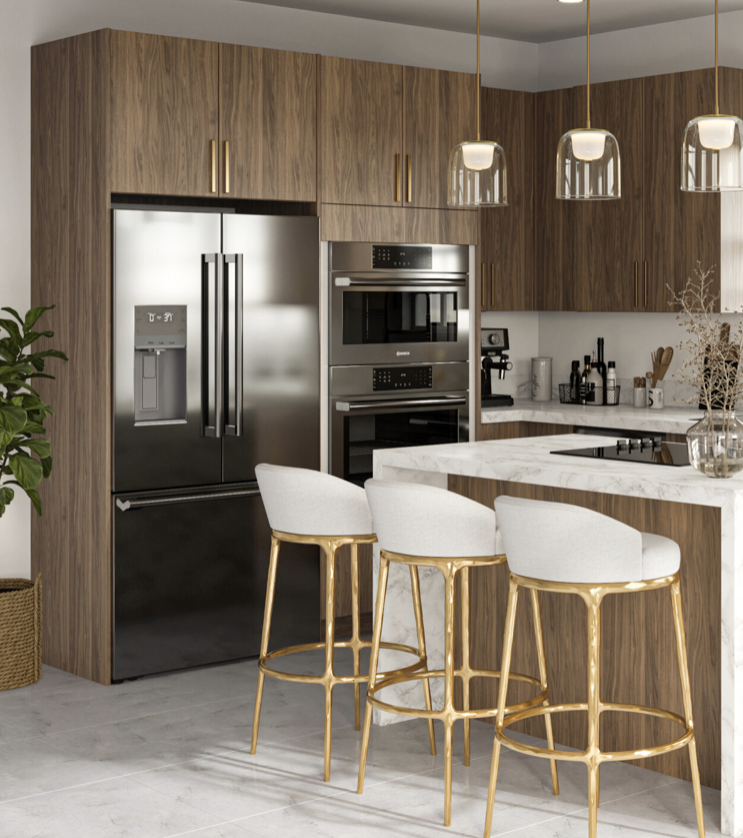 Modern kitchen with wooden cabinets, stainless steel refrigerator, built-in oven, and appliances. White marble countertop with three white and gold bar stools and pendant lights.